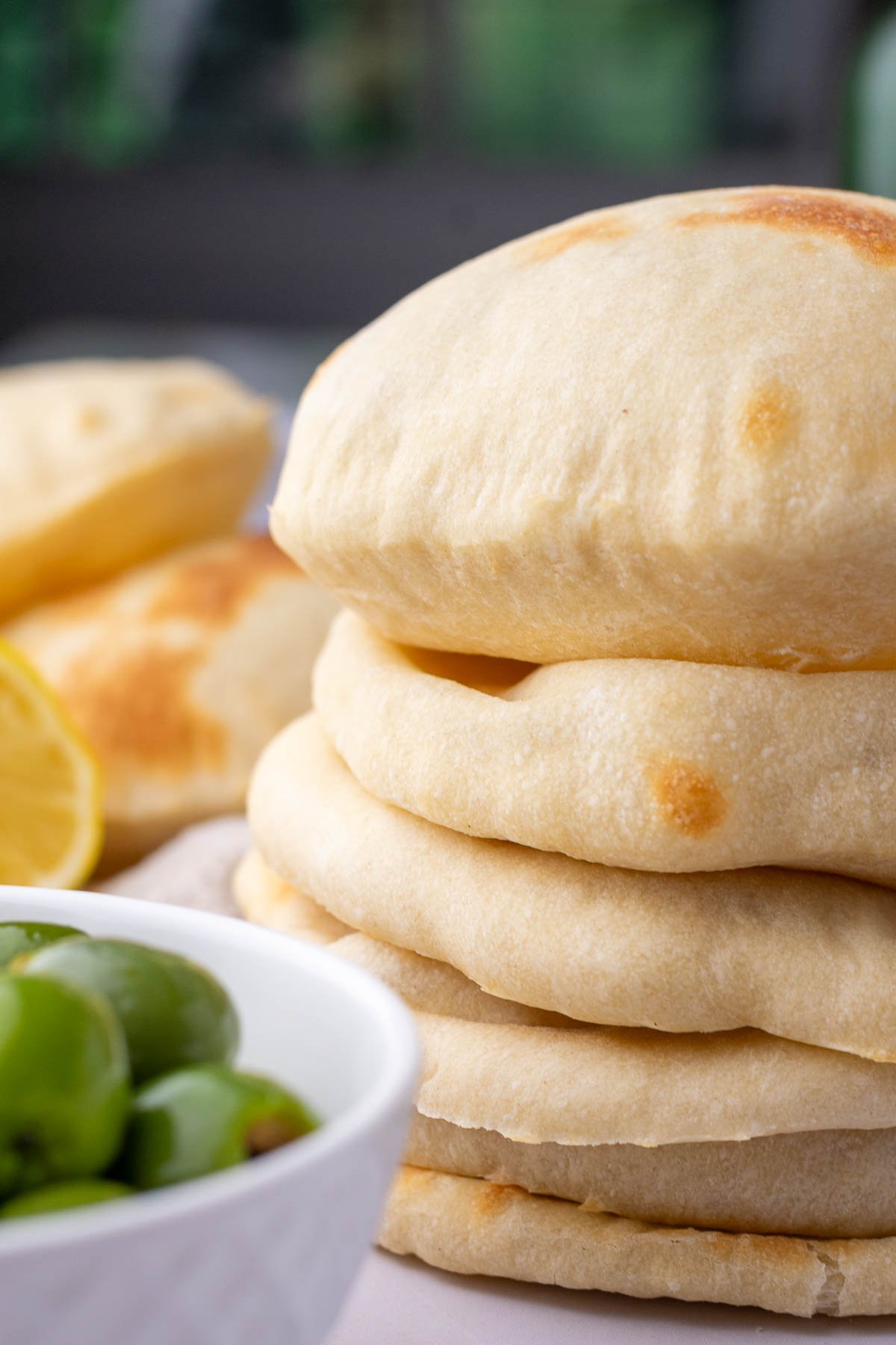 Stack of sourdough pita bread with a bowl of olives.