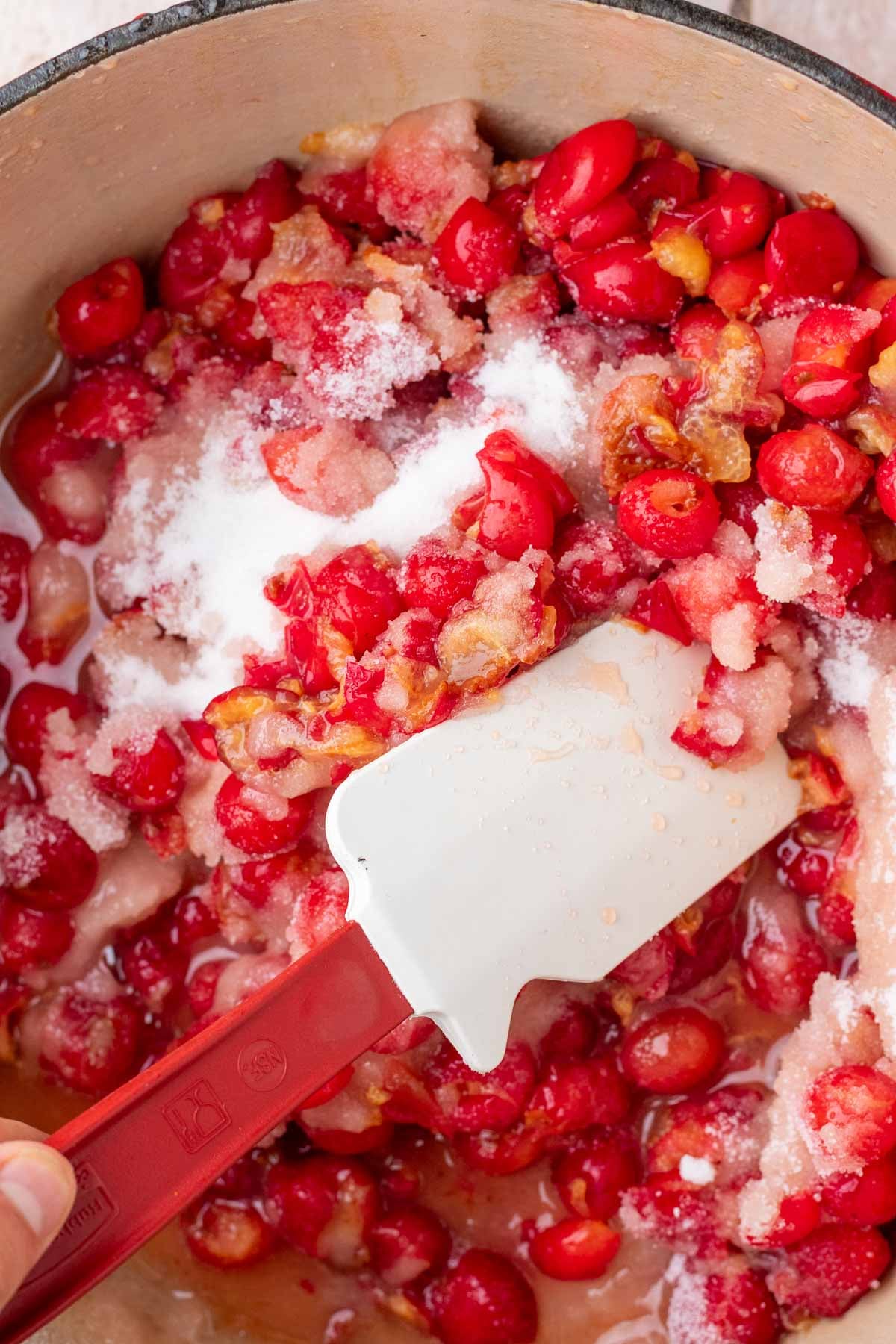 Stirring cherries with sugar in a large pot with a spatula.