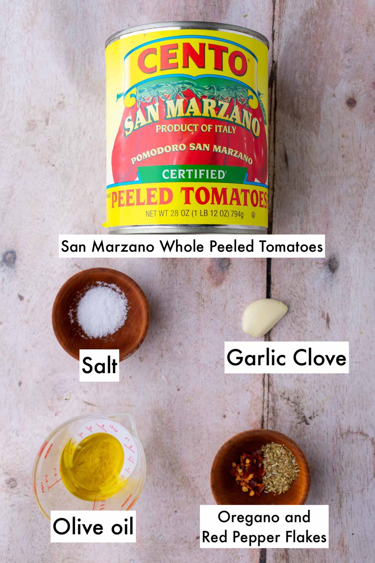 Labeled ingredients needed for easy pizza sauce including san marzano whole peeled tomatoes, garlic clove, salt, olive oil, oregano, and red pepper flakes.