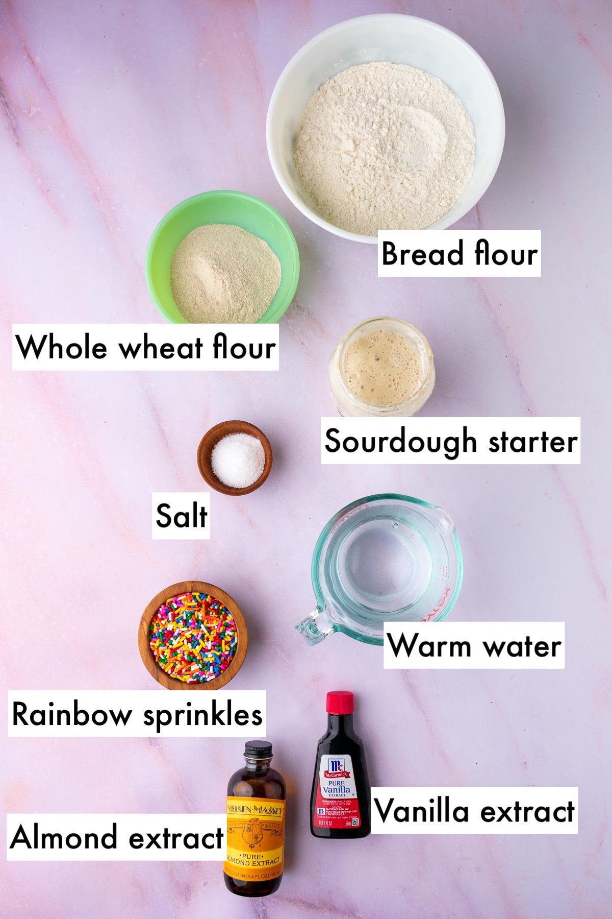Labeled ingredients needed for funfetti sourdough bread including bread flour, whole wheat flour, sourdough starter, salt, warm water, rainbow sprinkles, vanilla extract, and almond extract.