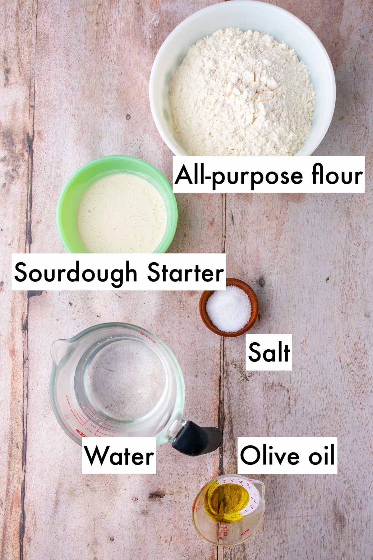 Labeled bowls of ingredients needed for sourdough pizza al taglio including all-purpose flour, sourdough starter, salt, water, and olive oil.