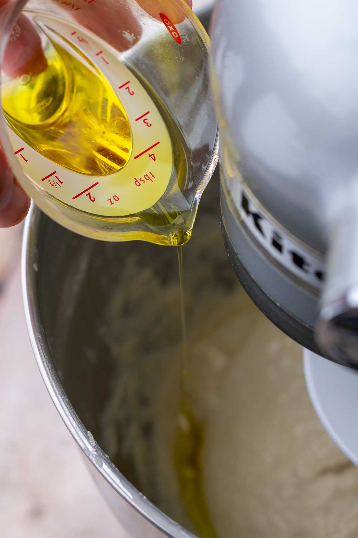 Pouring olive oil into bowl of stand mixer.