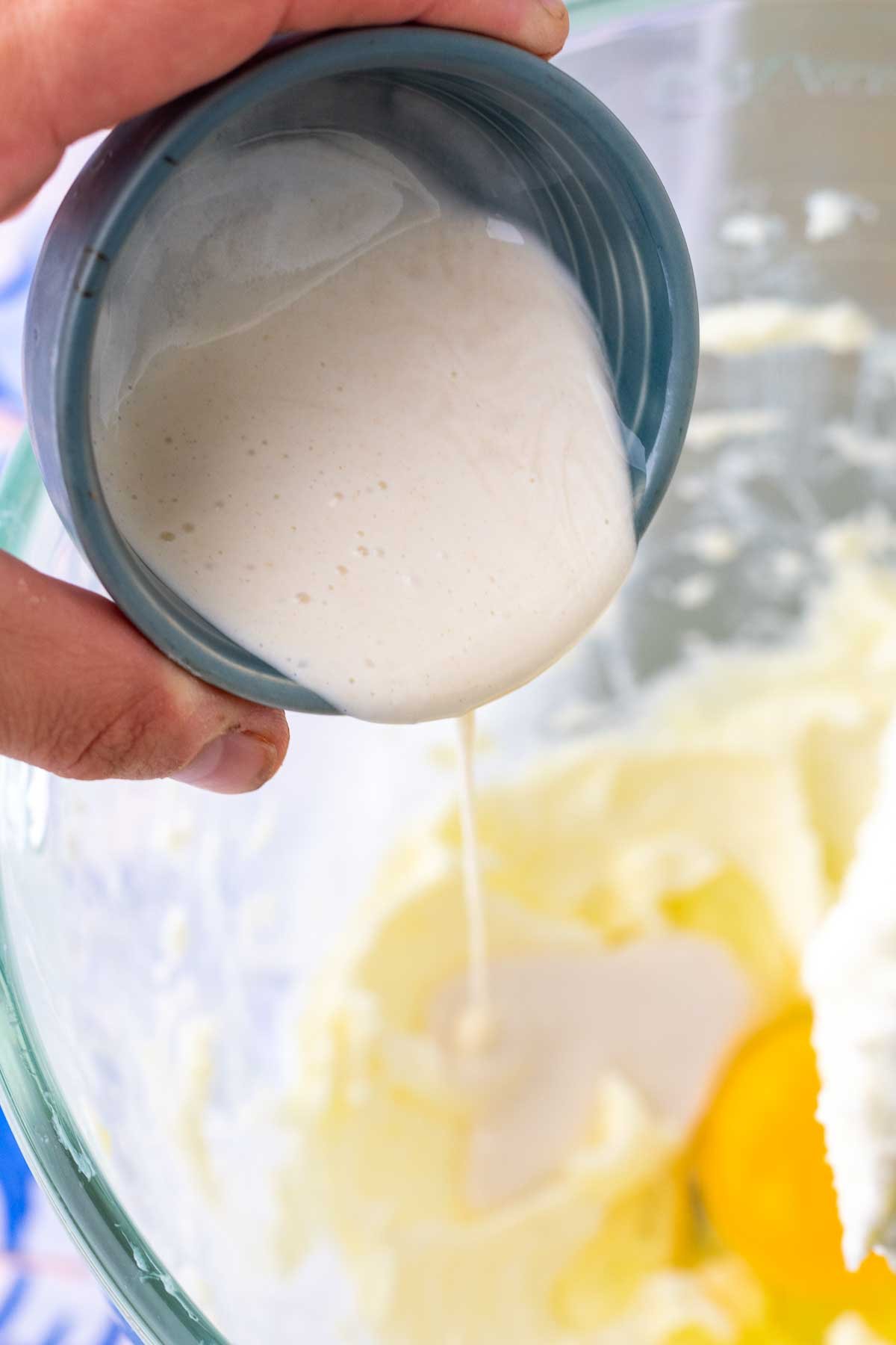 Hand pouring a small bowl of sourdough discard into a stand mixer.