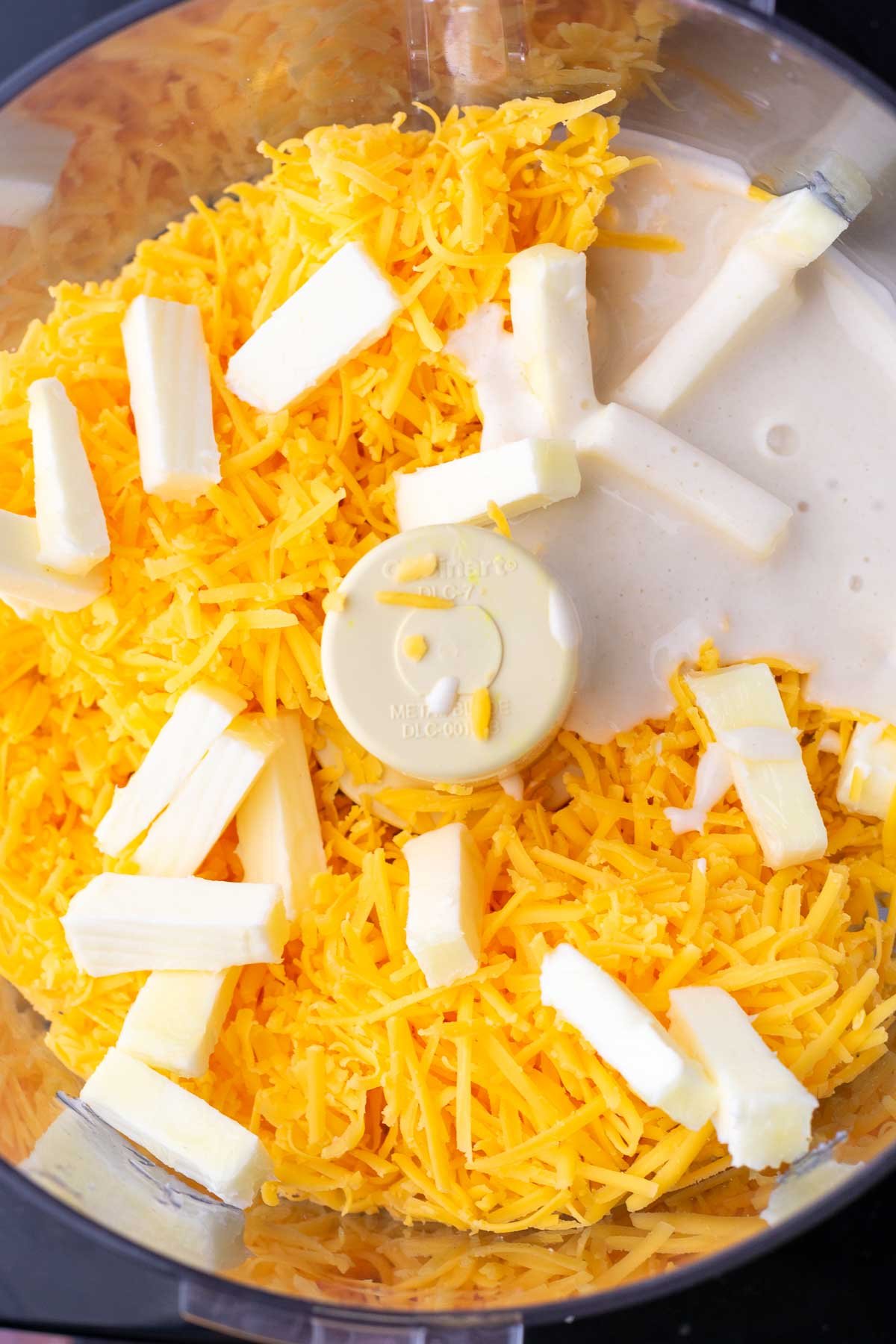 Shredded cheddar cheese, butter, and sourdough discard in a food processor.