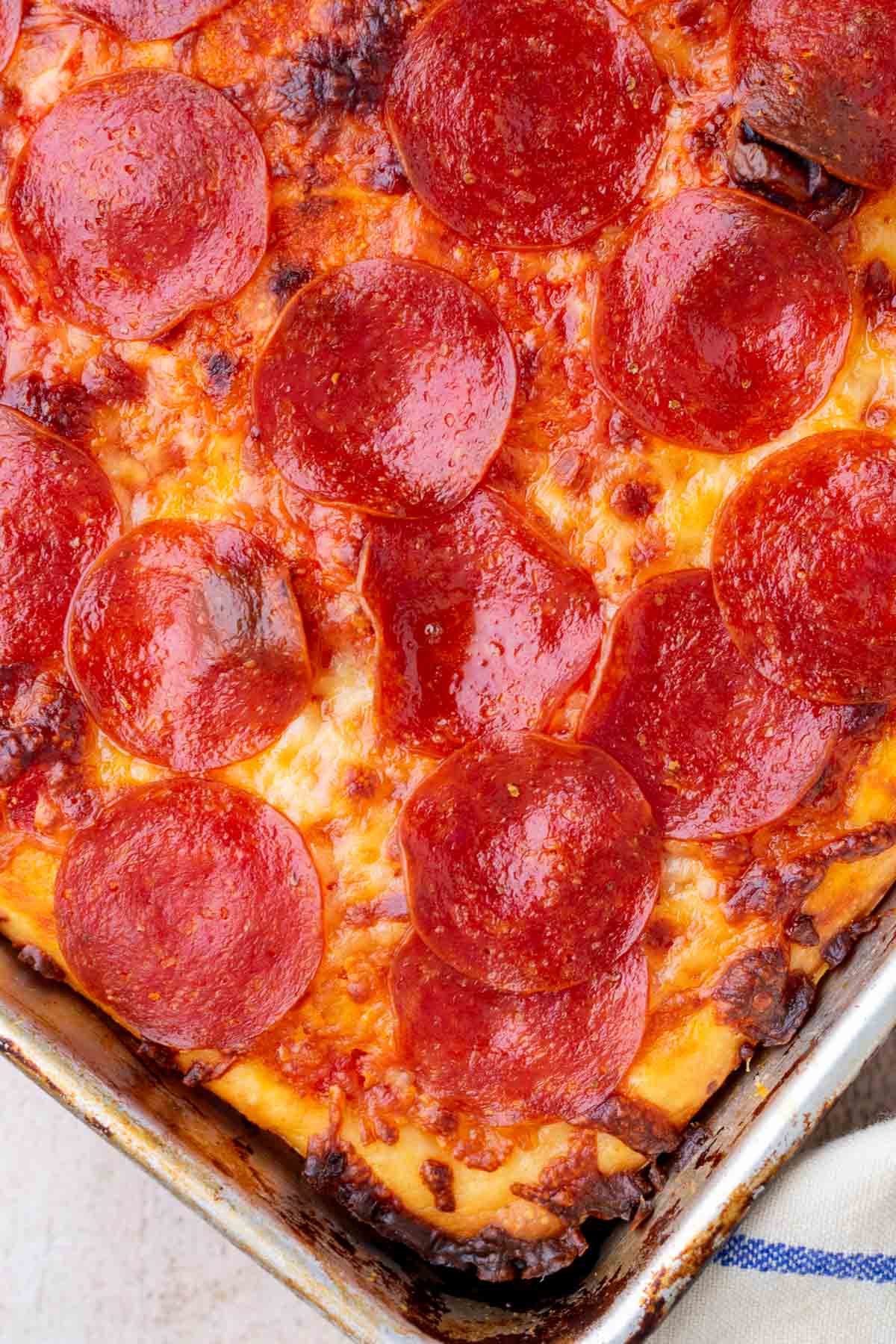 Close up of baked sourdough pizza al taglio in a sheet pan with pepperoni.