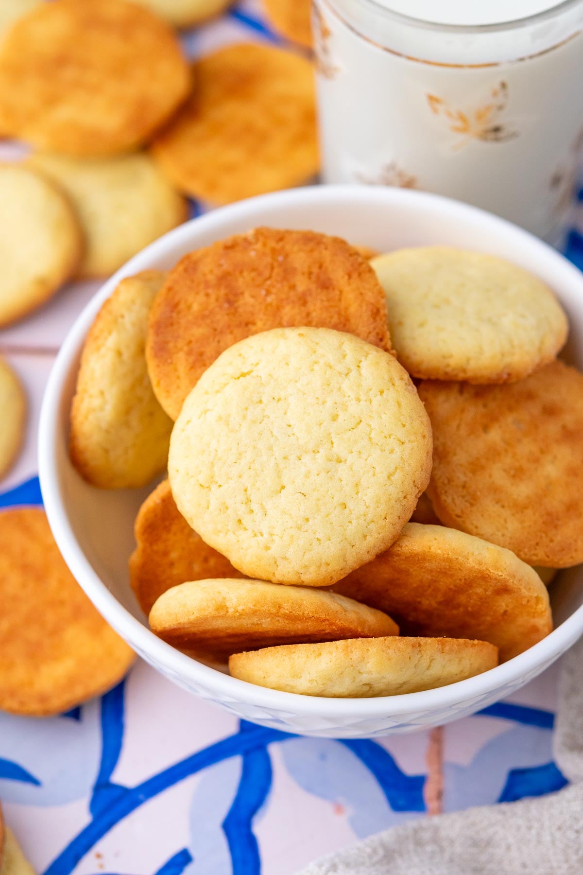 Close up of sourdough vanilla wafers in a bowl with a glass of milk.