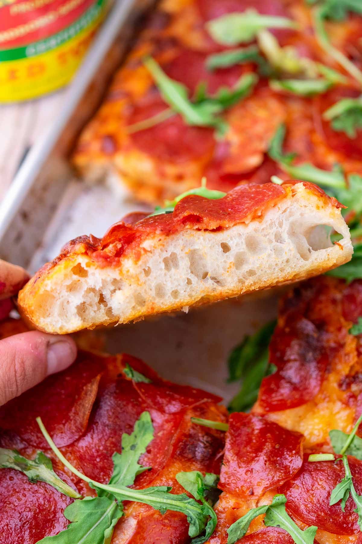 Hand holding a slice of sourdough pizza al taglio with visible open and airy crumb.