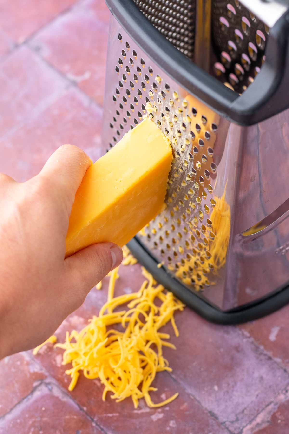 Hand grating a block of cheddar cheese on a box grater.