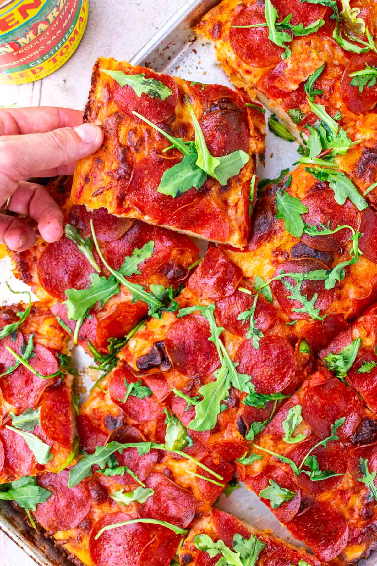 Hand picking a slice of Sourdough pizza al taglio from sheet pan.