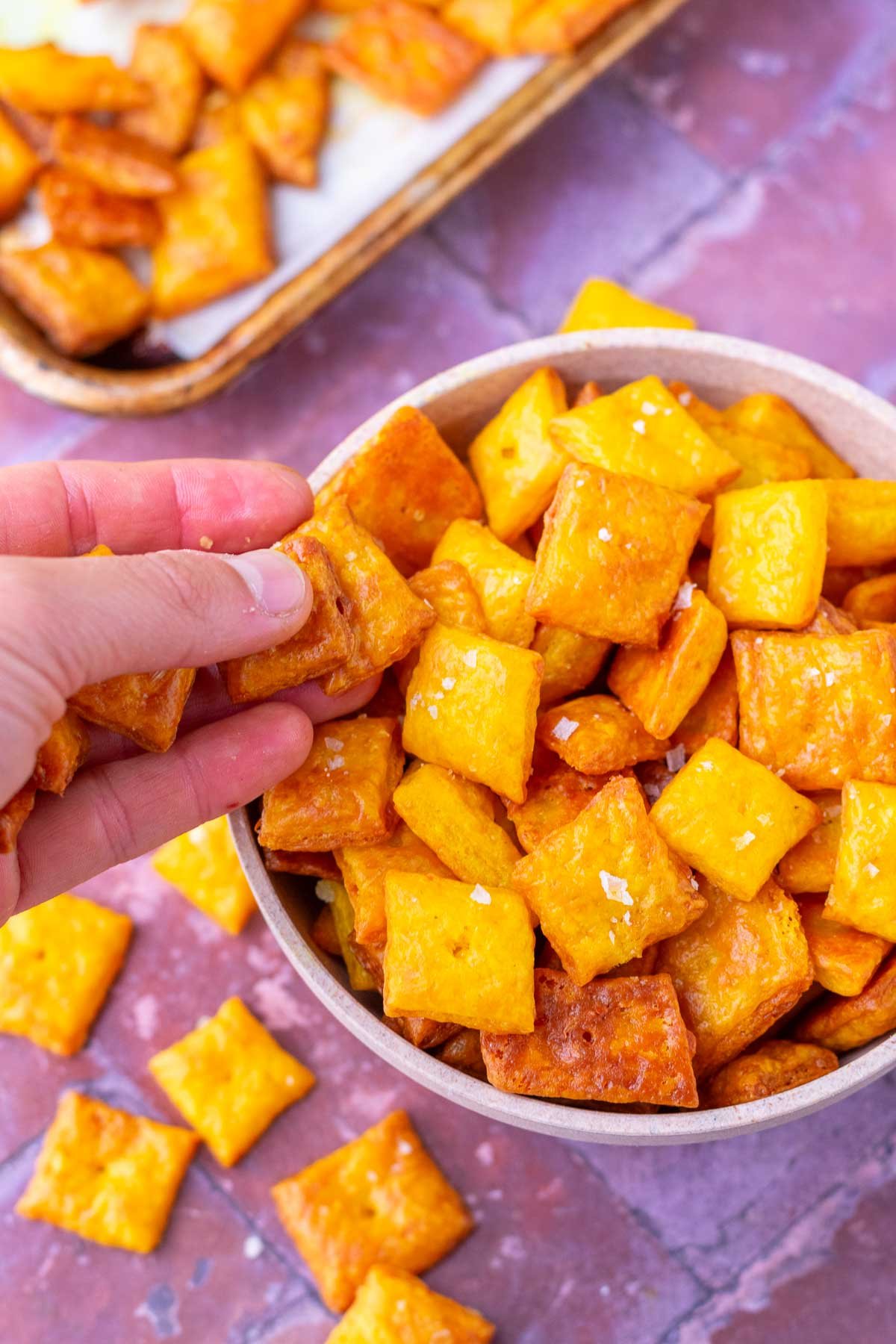Hand picking sourdough discard cheese crackers cheez-its from a bowl.