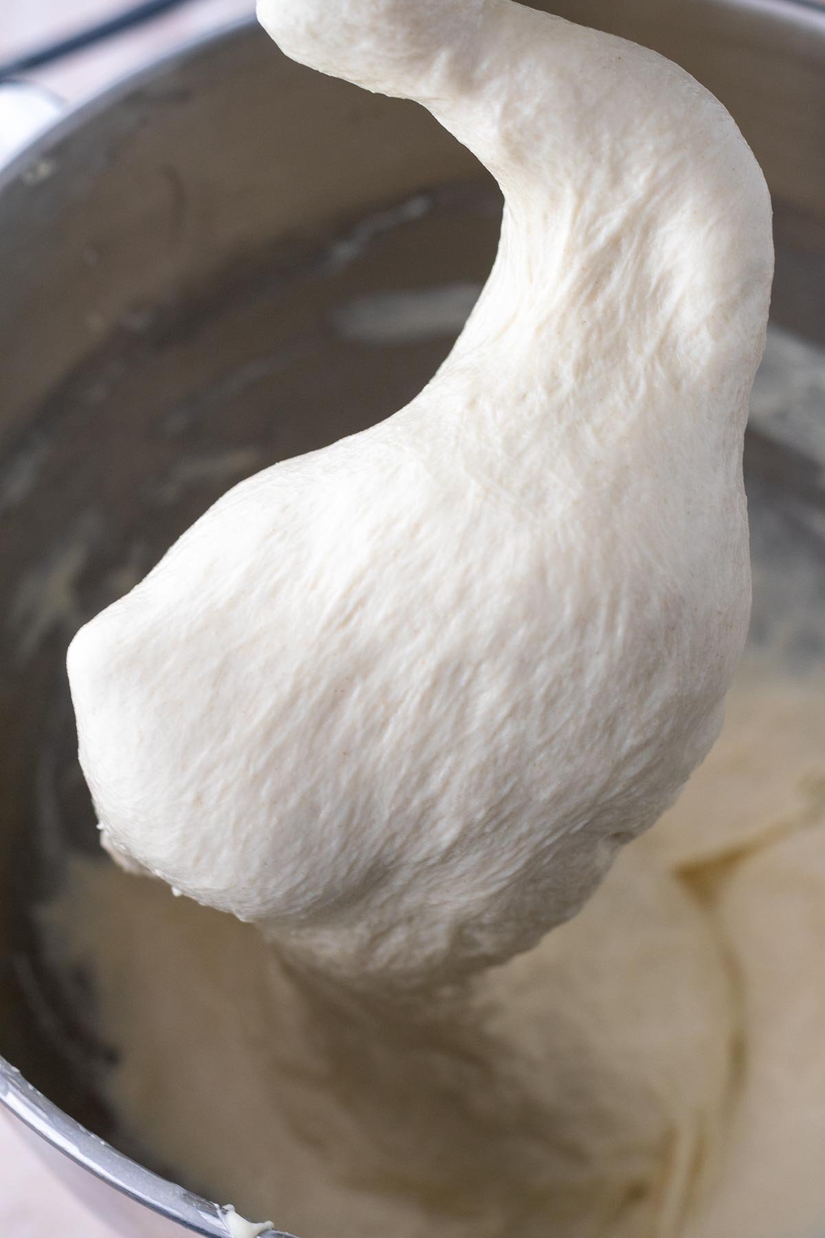 Mixed sourdough pizza al taglio dough in a bowl clinging to a dough hook.