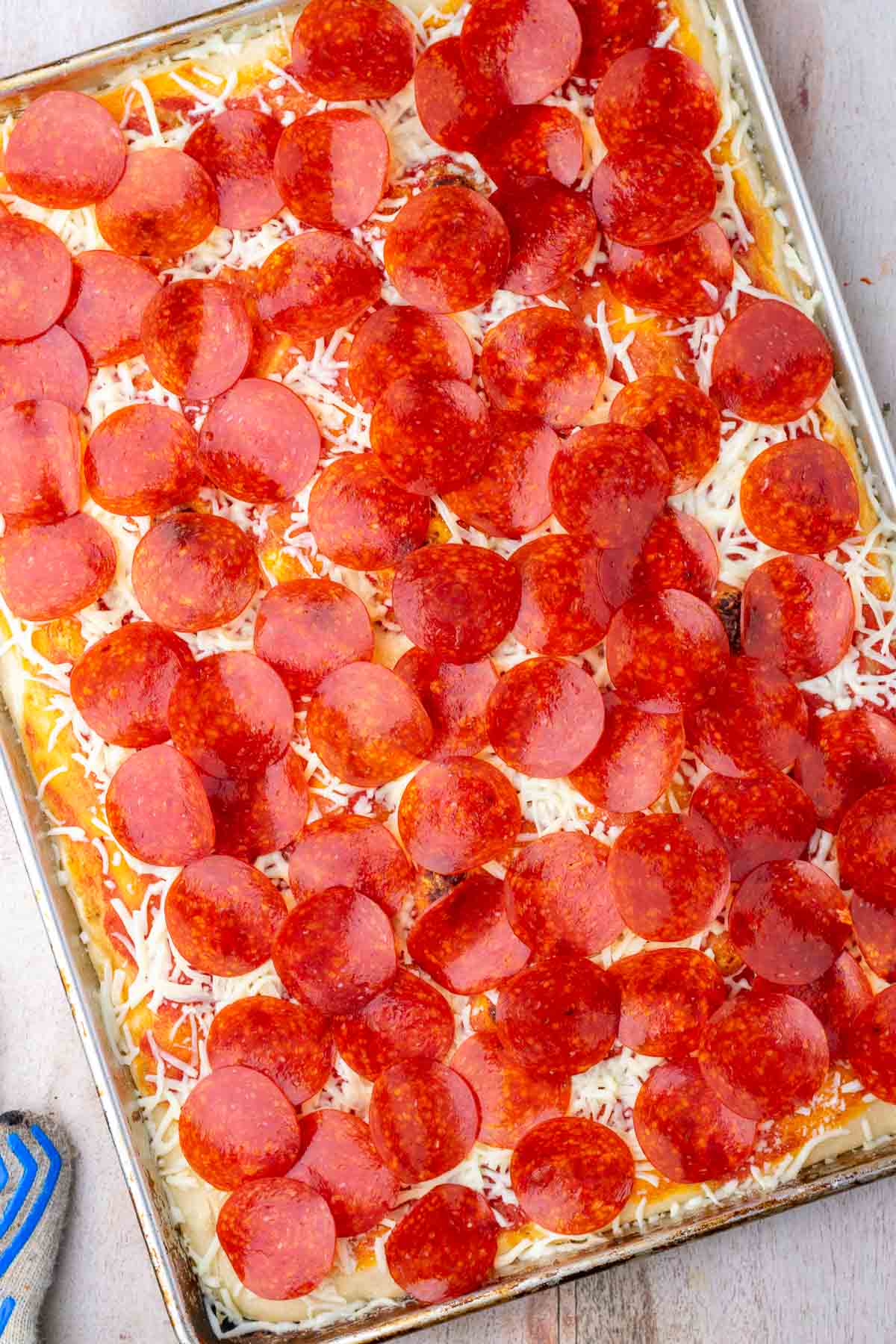 Pepperoni and mozzarella cheese added to sourdough sheet pan pizza before baking.