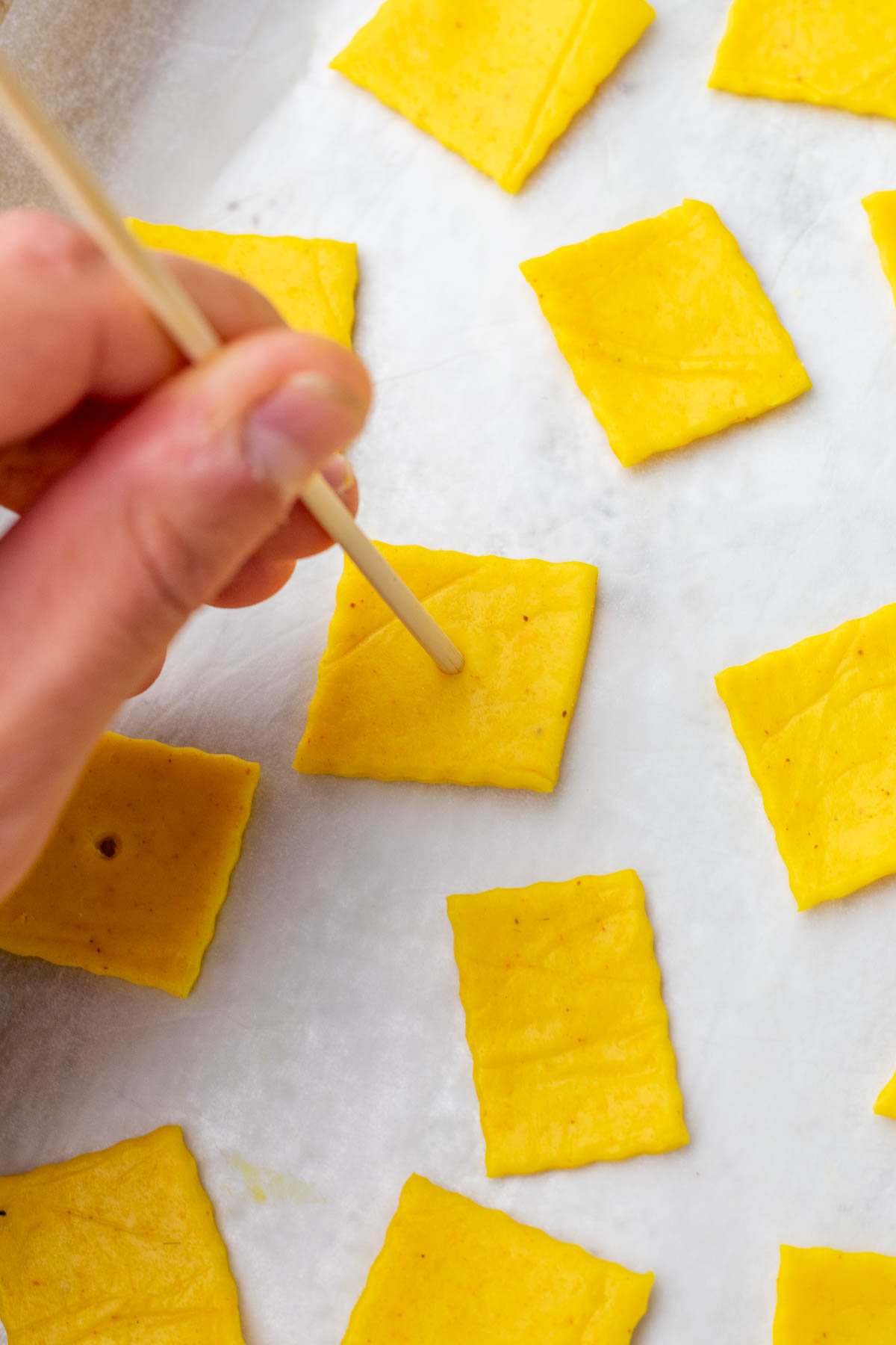 Docking sourdough discard cheese crackers with a wooden dowel.