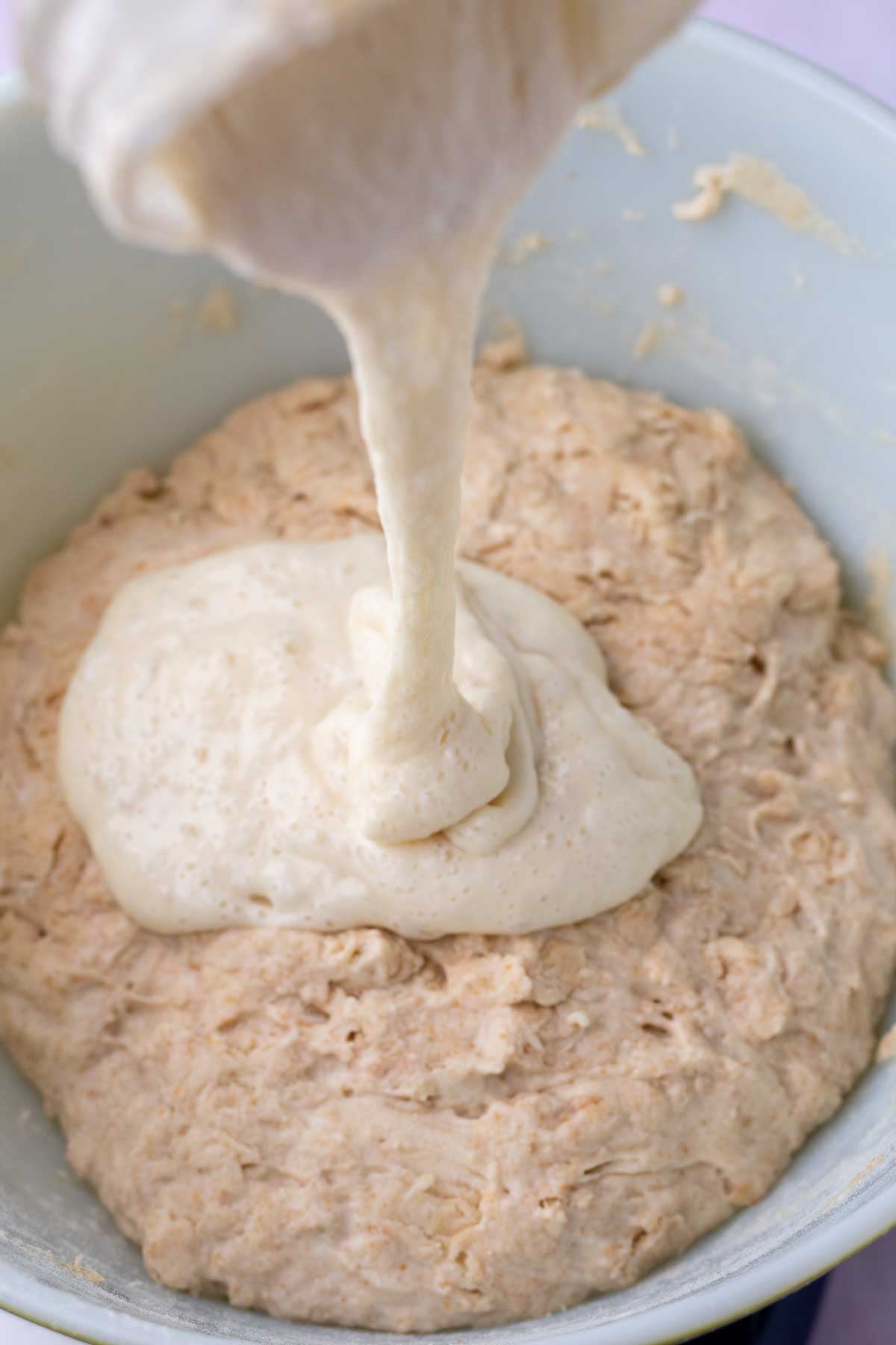 Pouring sourdough starter into a bowl with bread dough.