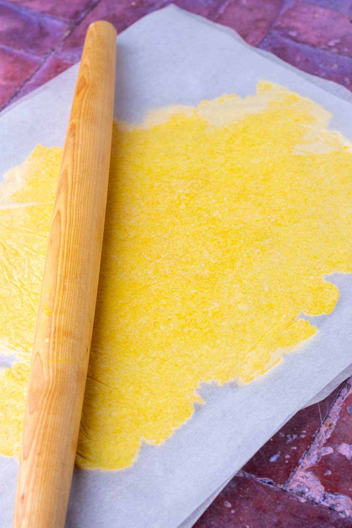 Rolling pin rolling out sourdough discard cheese crackers in between parchment paper.