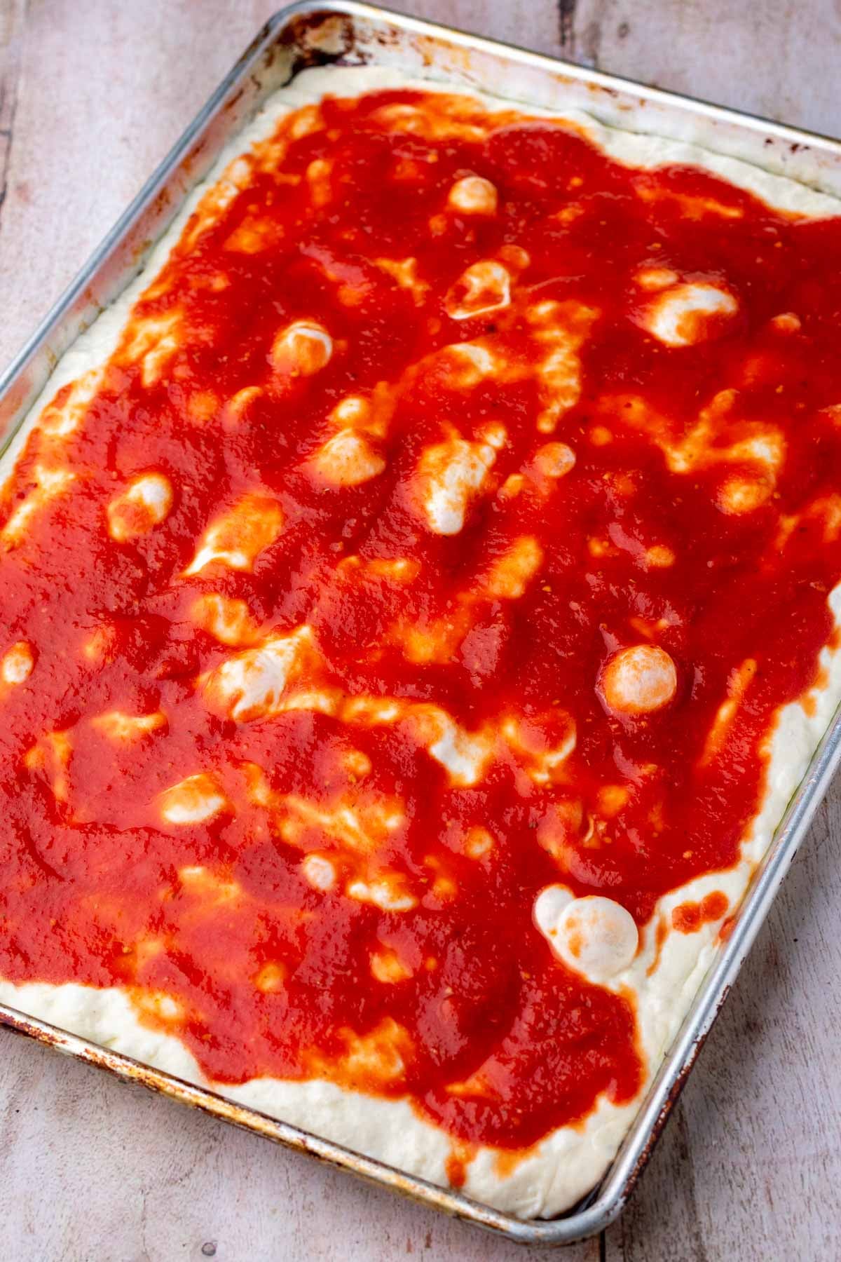 Pizza sauce added on top of sheet pan sourdough pizza dough.