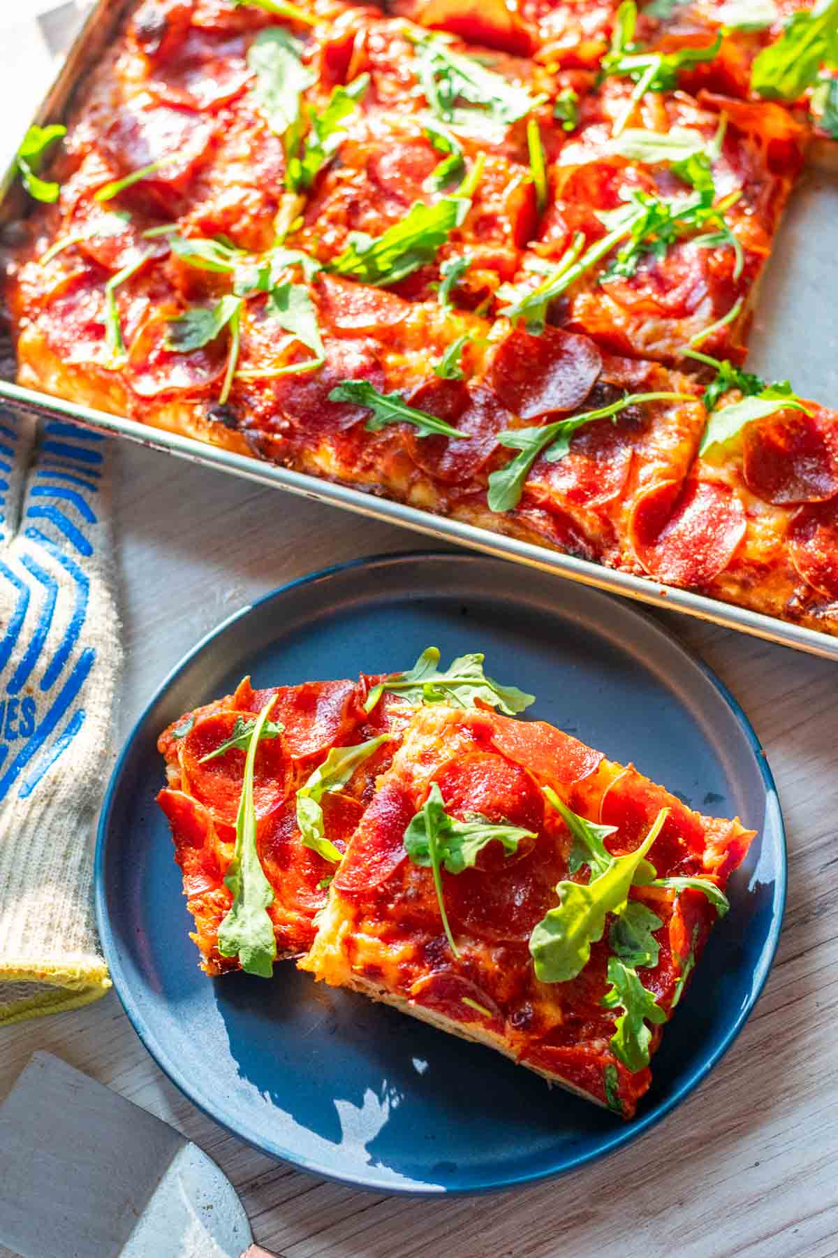 Slices of sourdough pizza al taglio in a sheet pan and a couple slices on a plate.