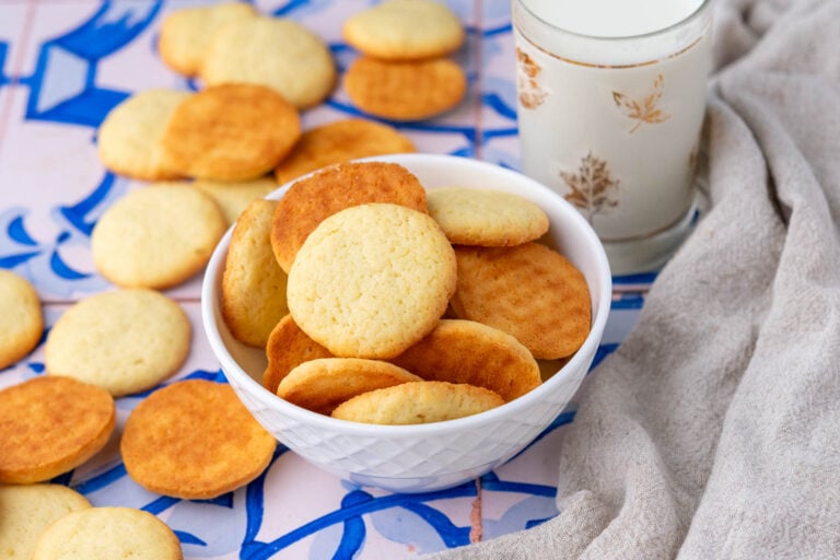 Bowl of sourdough vanilla wafers with a glass of milk surrounded by sourdough nilla wafers and a towel.