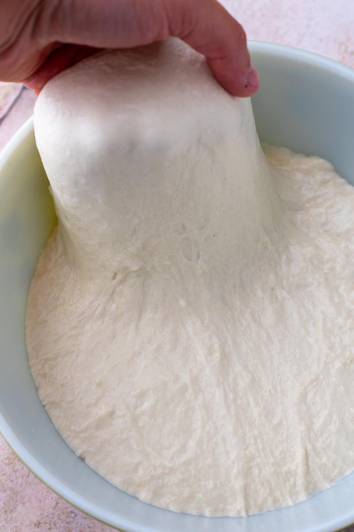 Hand stretching sourdough pizza al taglio dough in bowl.