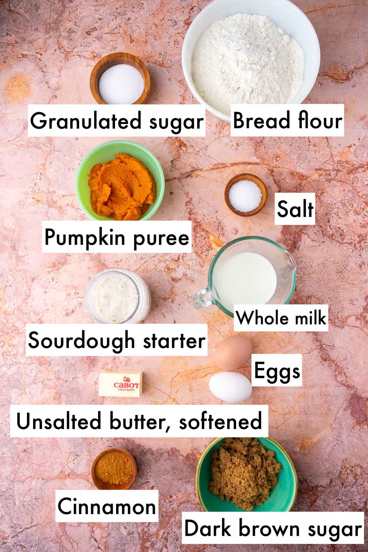 Labeled ingredients needed for sourdough pumpkin cinnamon swirl bread including bread flour, granulated sugar, salt, pumpkin puree, whole milk, eggs, unsalted butter, cinnamon, sourdough starter, and dark brown sugar.