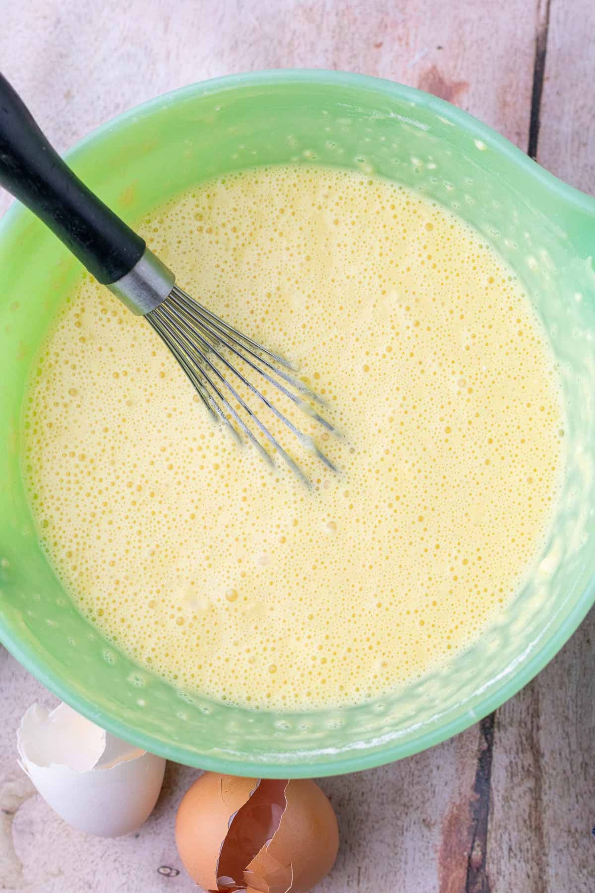 Mixed cheesy sourdough popover batter in a bowl with a whisk.