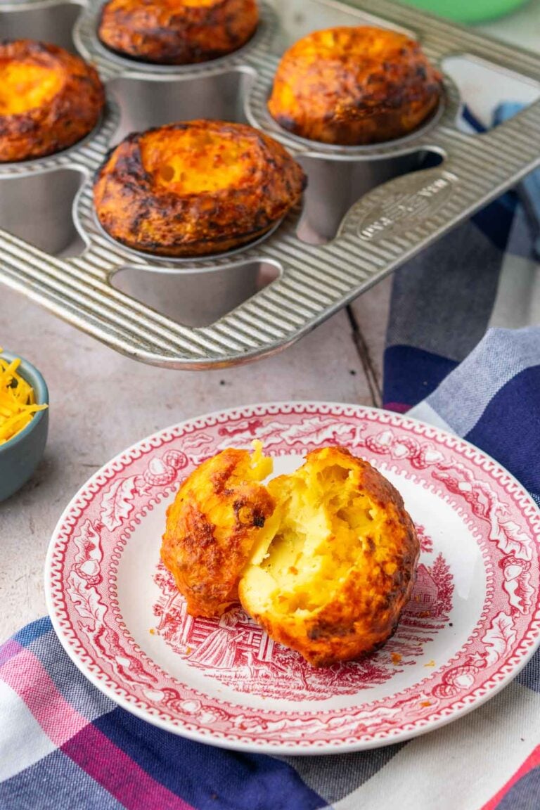 Cheesy sourdough popover torn on a plate with popovers in pan in the background.