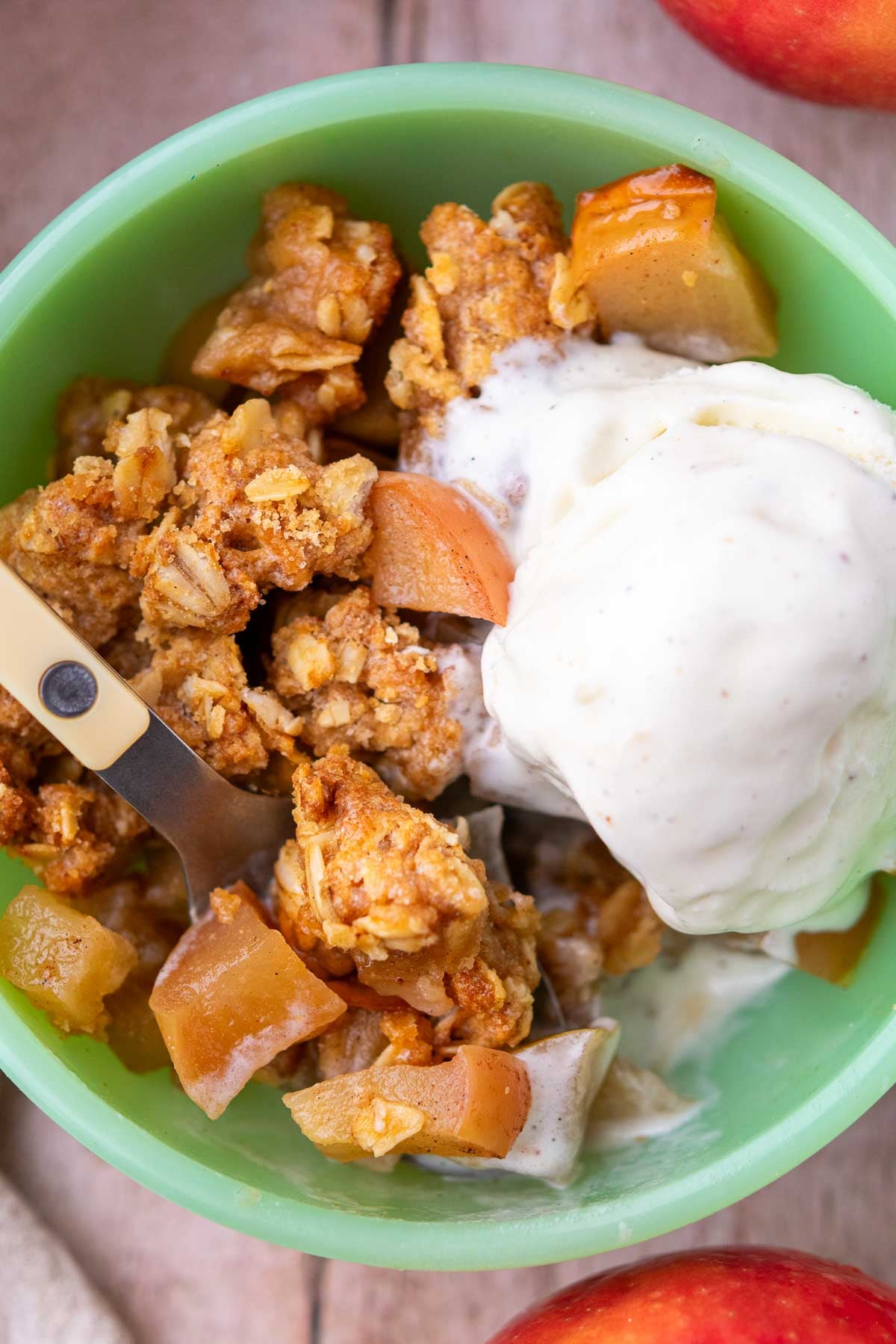Close up of sourdough apple crisp in a bowl with a scoop of ice cream and a spoon.
