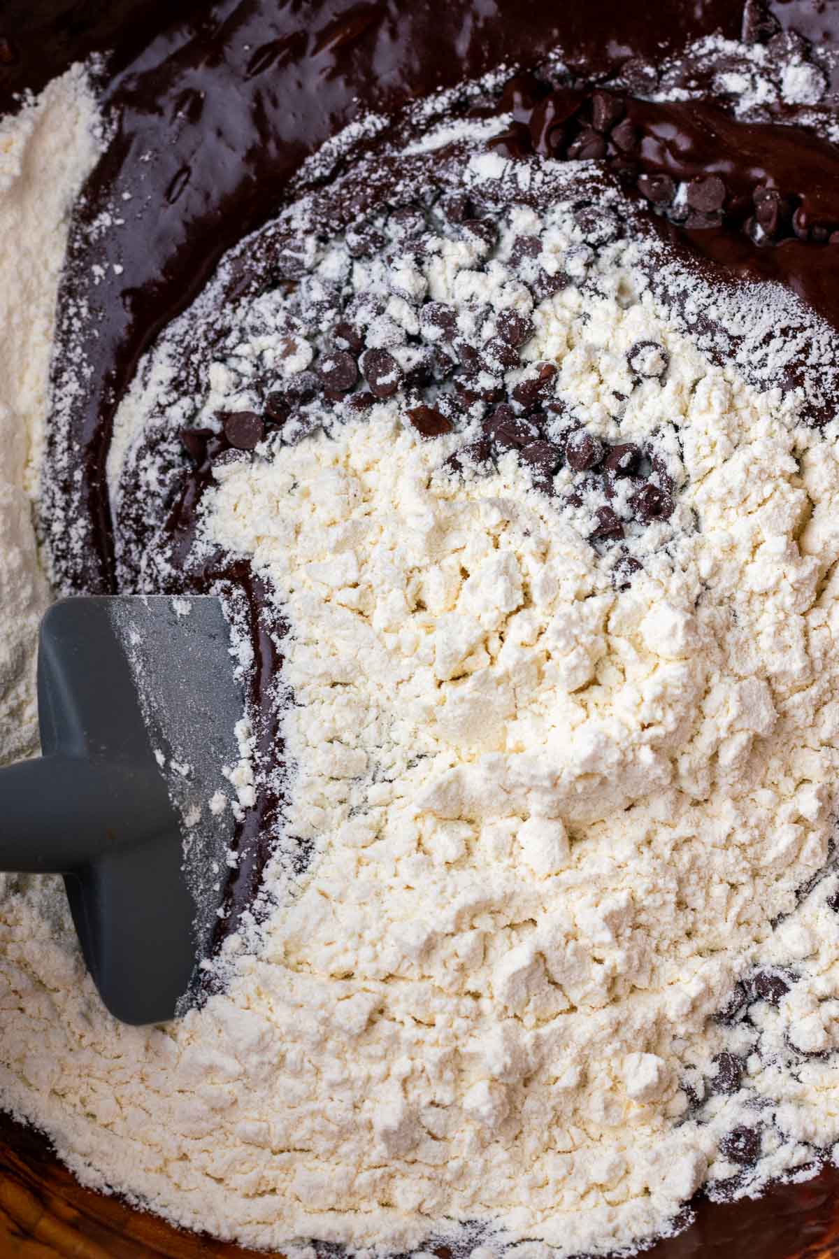 Folding flour and chocolate chips in sourdough brownie batter with a spatula in a bowl.
