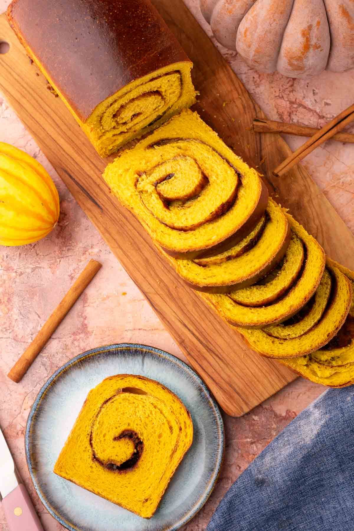 Sliced sourdough pumpkin cinnamon swirl bread on cutting board surrounded by pumpkins.
