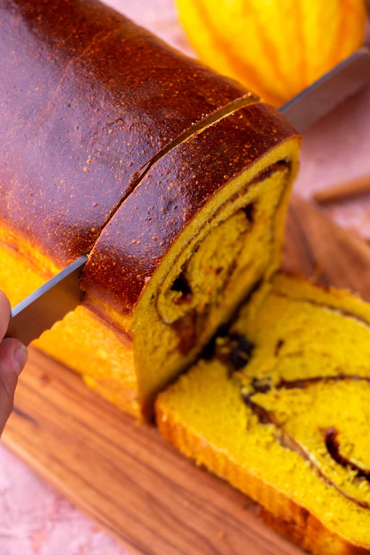 Bread knife slicing a loaf of sourdough pumpkin cinnamon swirl bread.