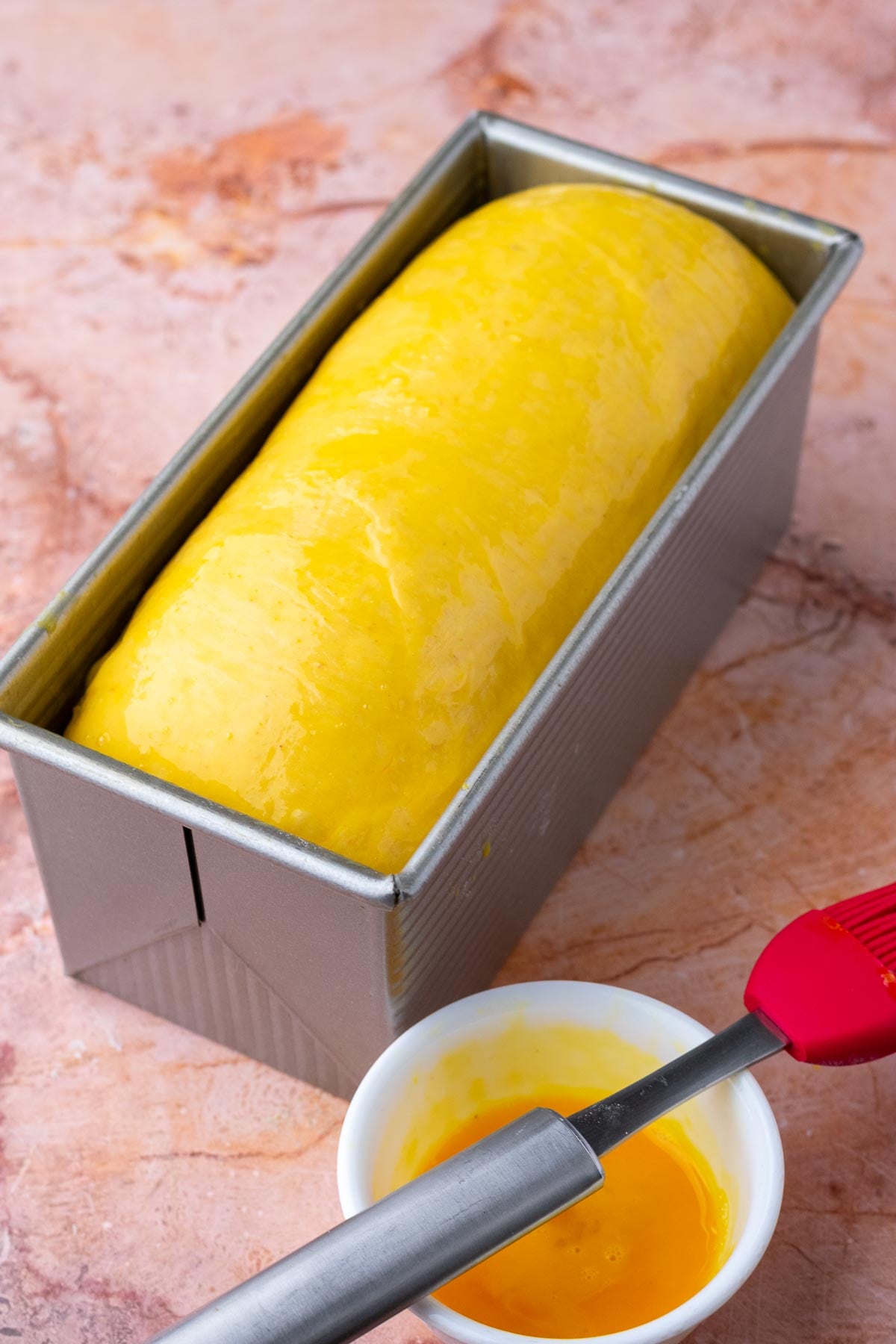 sourdough pumpkin cinnamon swirl bread in bread loaf pan at the end of final proof brushed with egg wash.