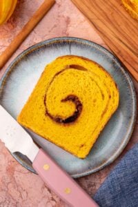 Slice of sourdough pumpkin cinnamon swirl bread on a plate with a bread knife.