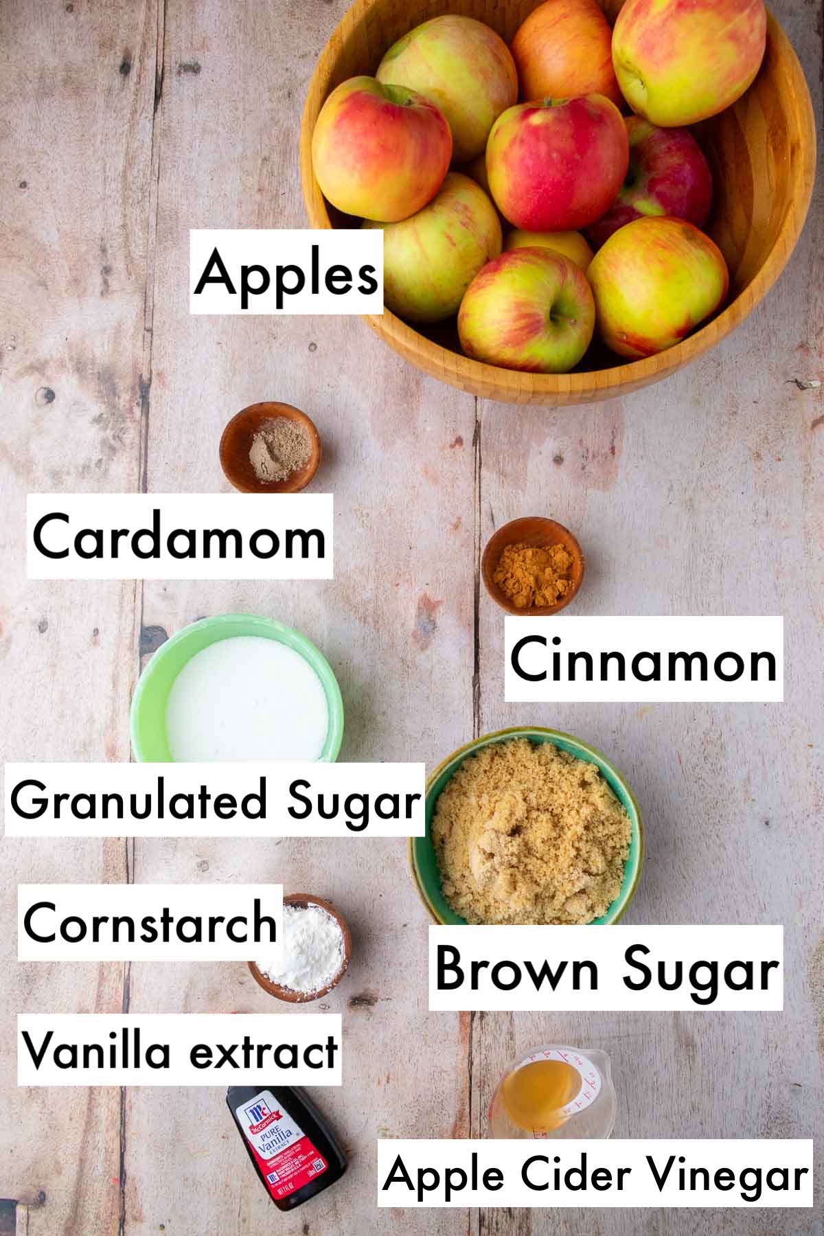 Labeled ingredients needed for sourdough apple pie filling including apples, cinnamon, cardamom, granulated sugar, brown sugar, apple cider vinegar, cornstarch, and vanilla extract.