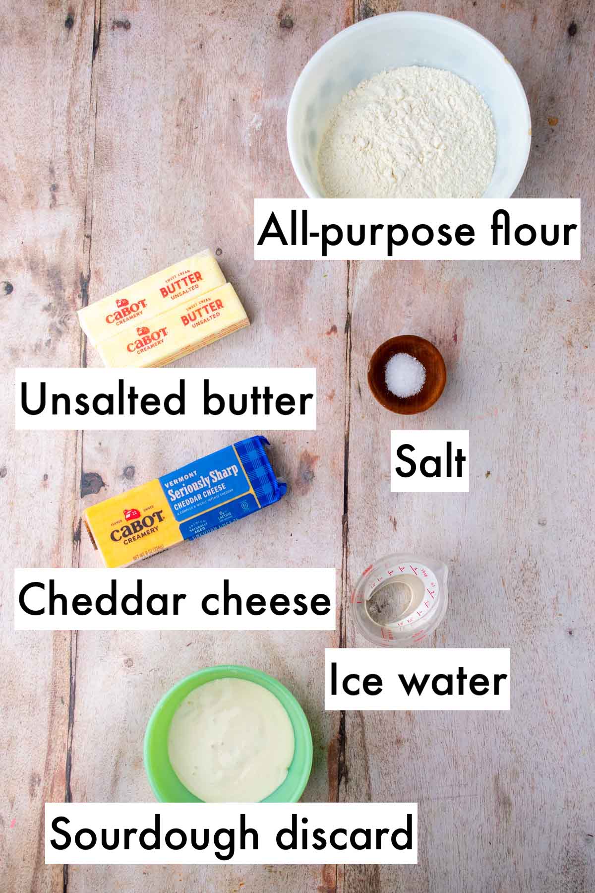 Labeled ingredients needed for sourdough cheddar pie crust including all-purpose flour, unsalted butter, salt, cheddar cheese, ice water, and sourdough discard.
