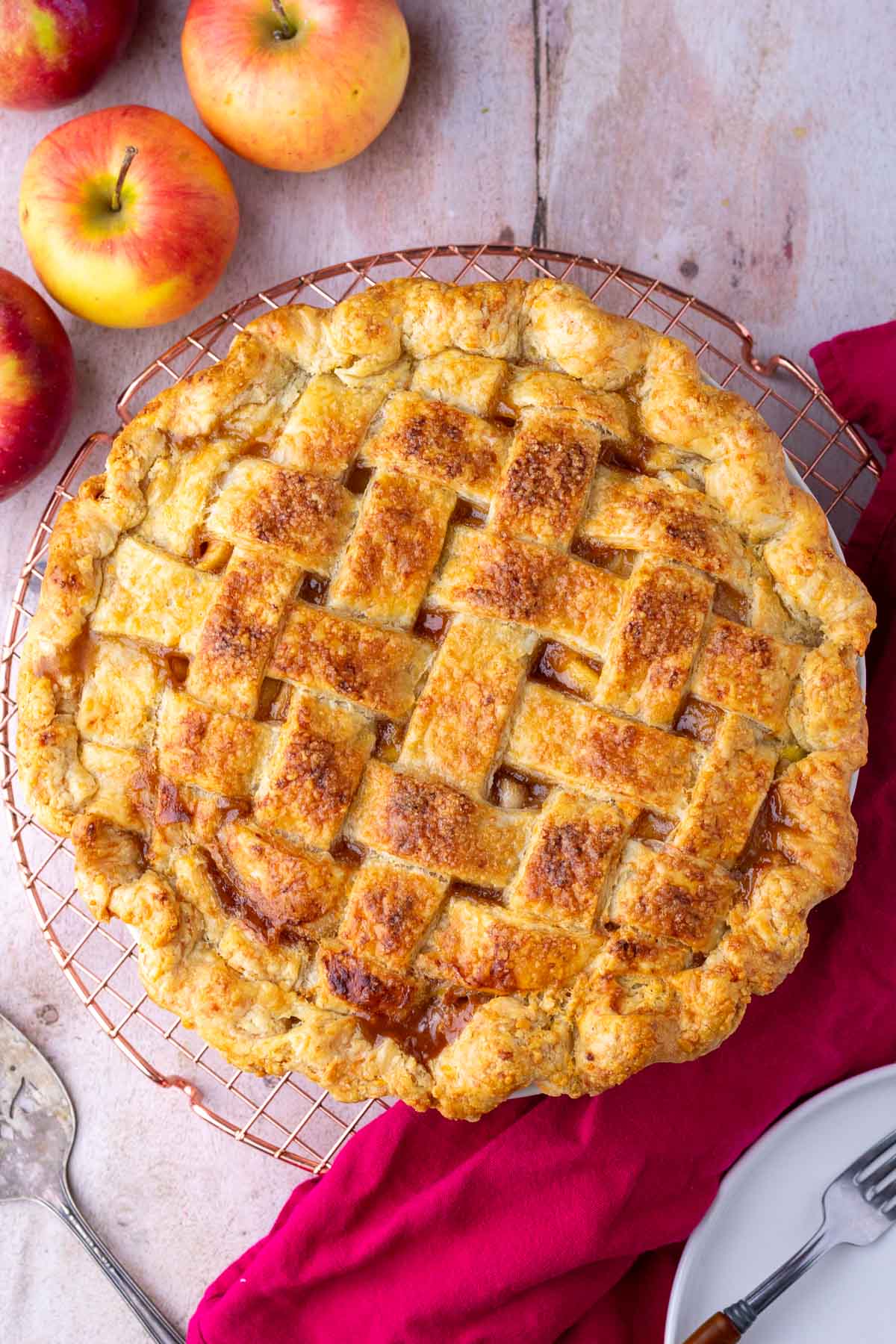 Baked sourdough apple pie on a wire rack with apples around it.