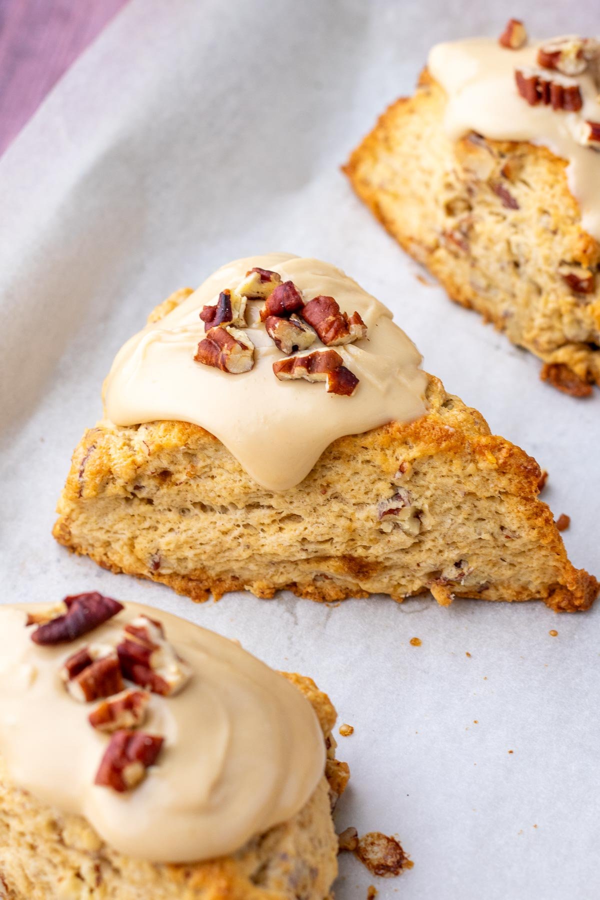 Baked sourdough maple pecan scones on a sheet pan with a salted maple glaze and pecans on top.