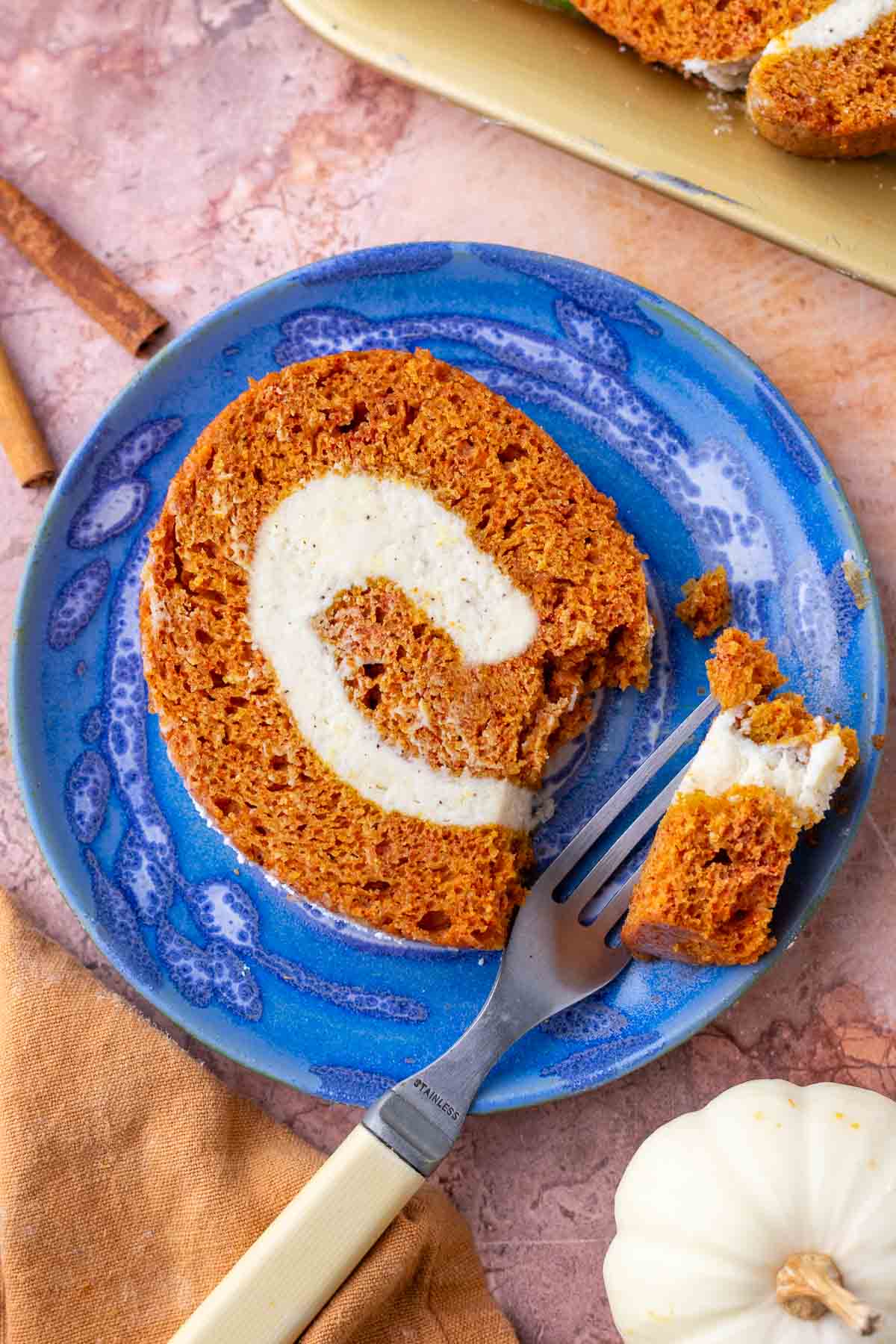 Slice of sourdough pumpkin roll with brown butter cream cheese on a plate with a fork and bite taken out of it.