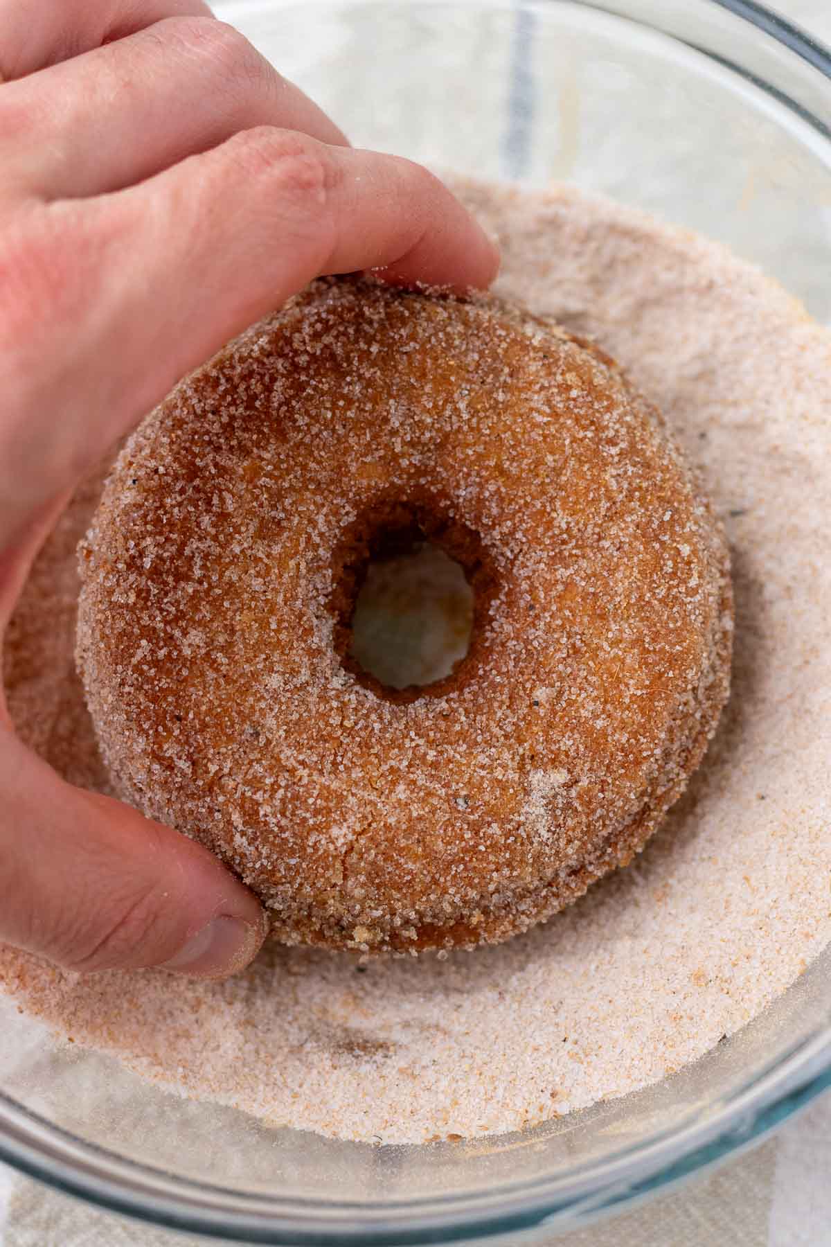 Tossing sourdough pumpkin donut in a bowl of pumpkin spice sugar.