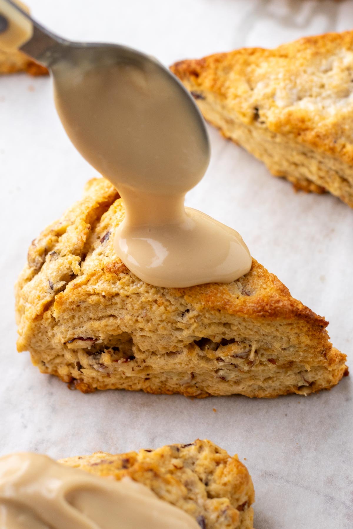 Spooning salted maple glaze on a sourdough maple pecan scone.