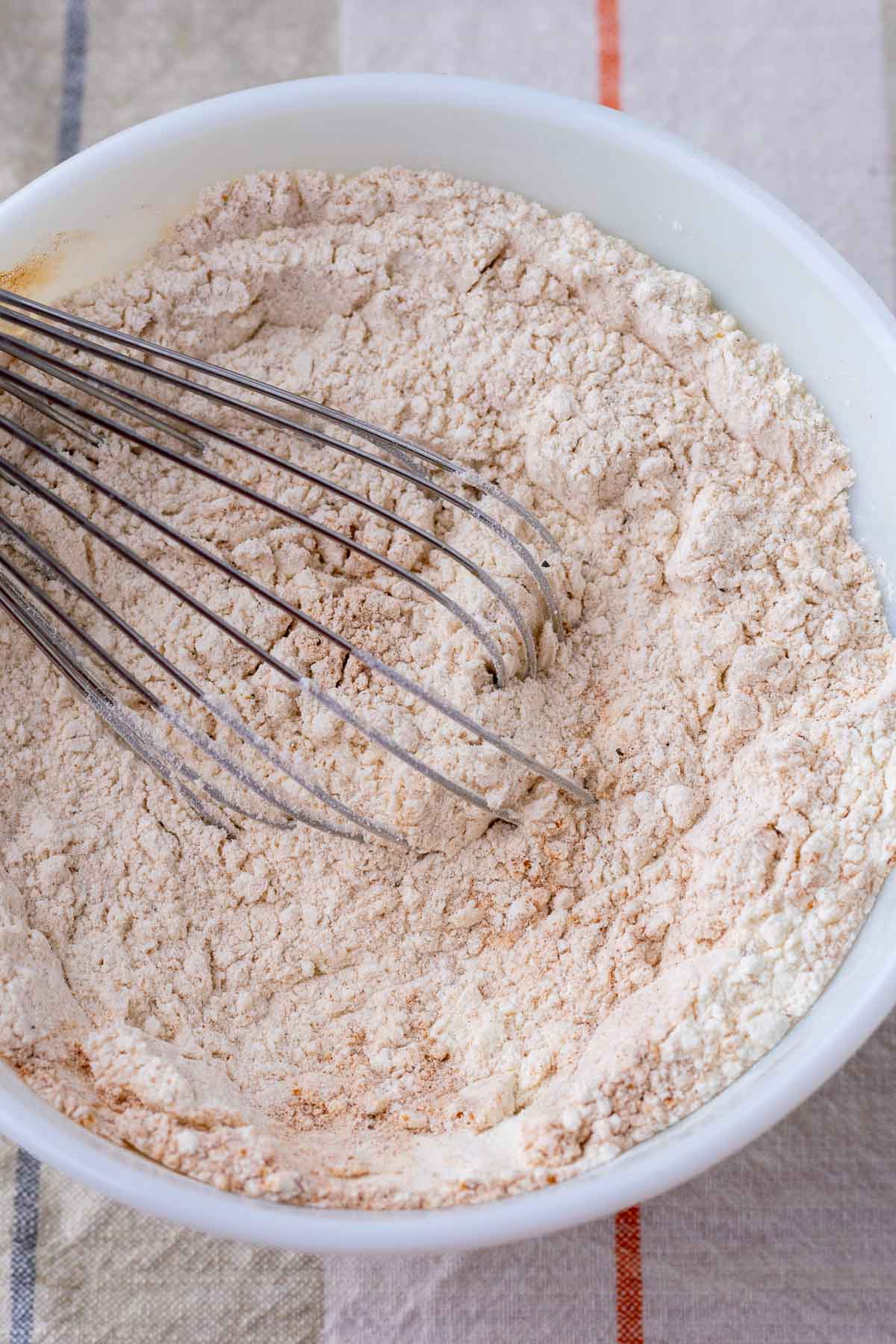 Mixing dry ingredients for sourdough pumpkin donuts in a bowl with a whisk.