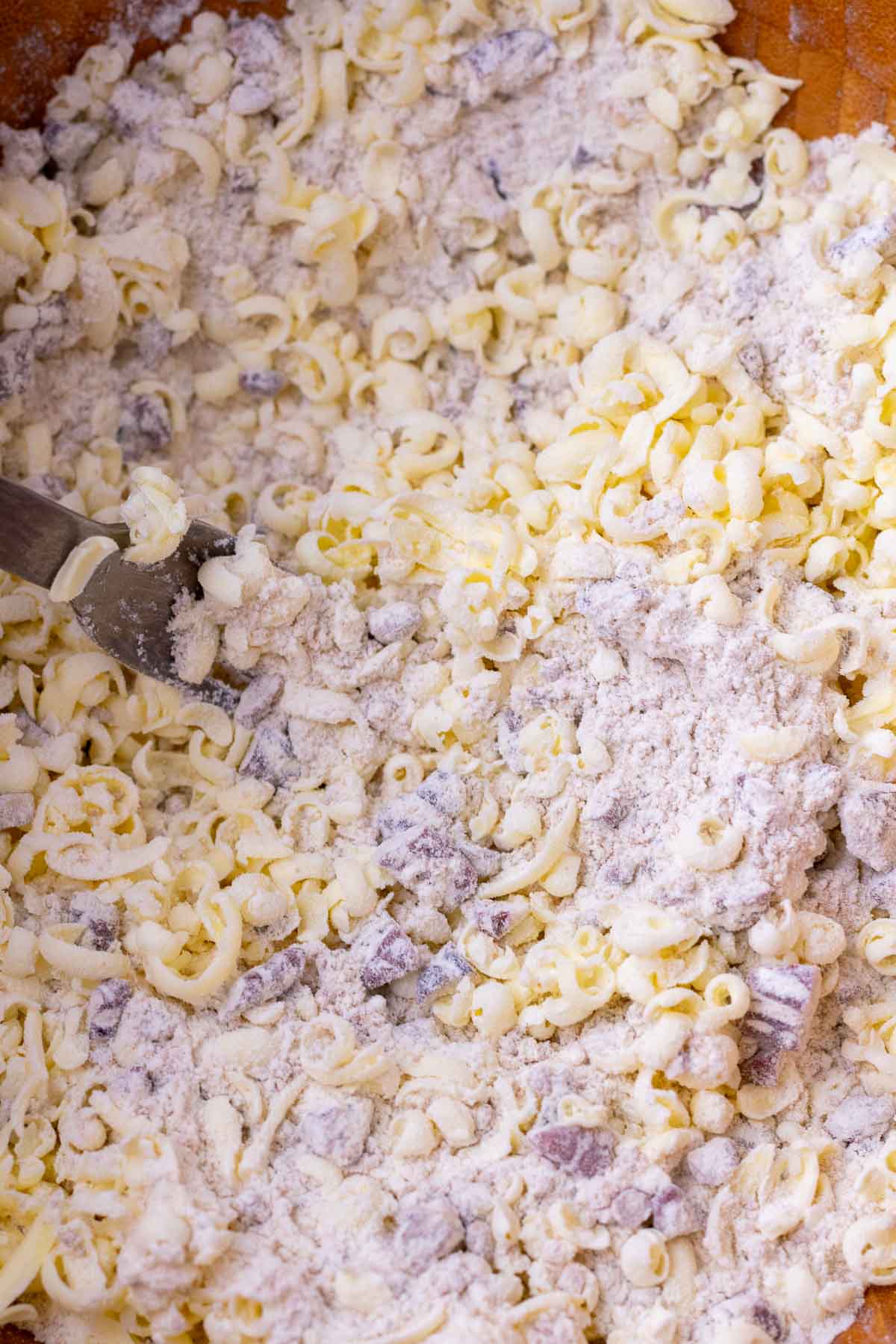 Fork tossing grated butter for sourdough maple pecan scones in a bowl.