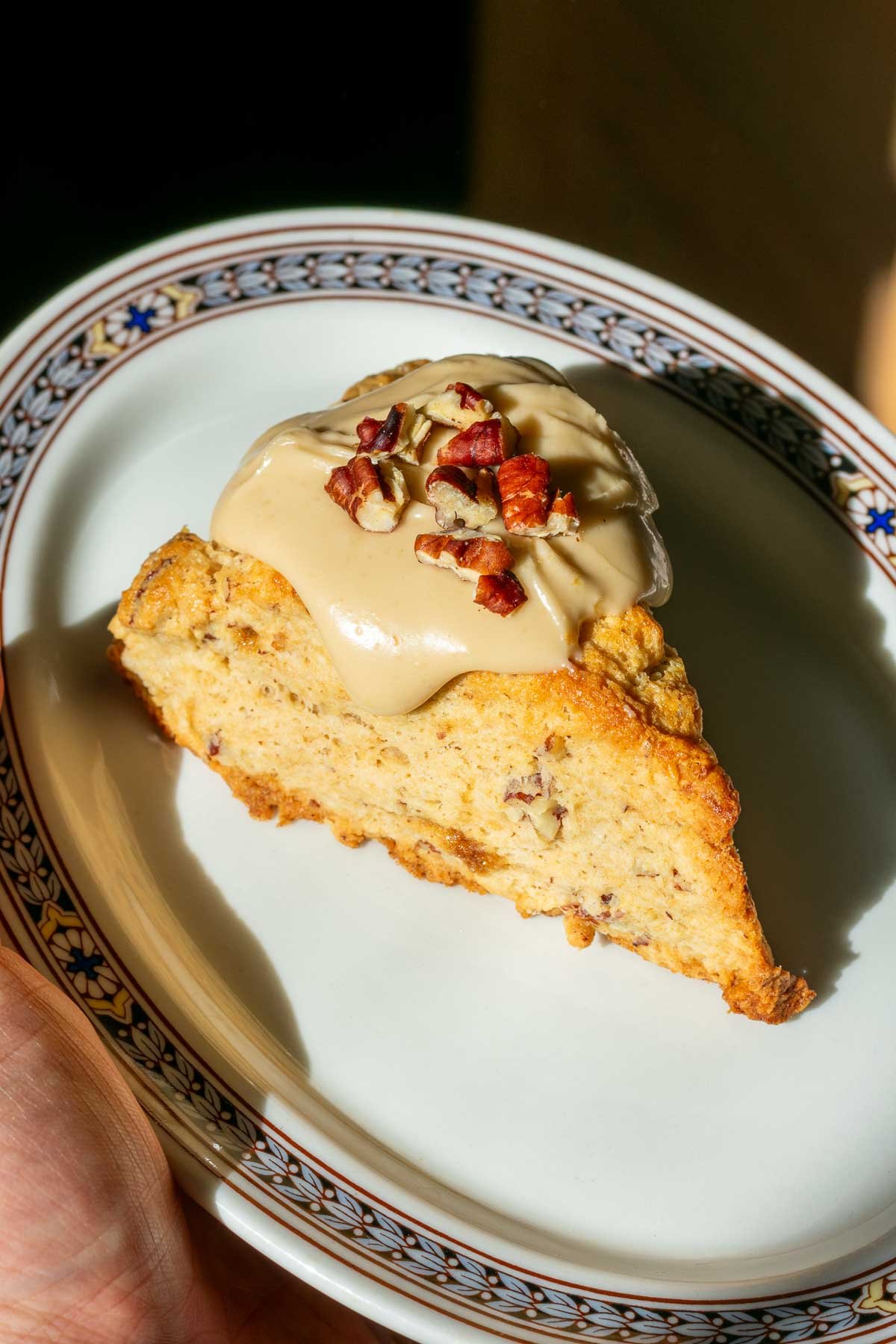 Hand holding a plate with a sourdough maple pecan scone.