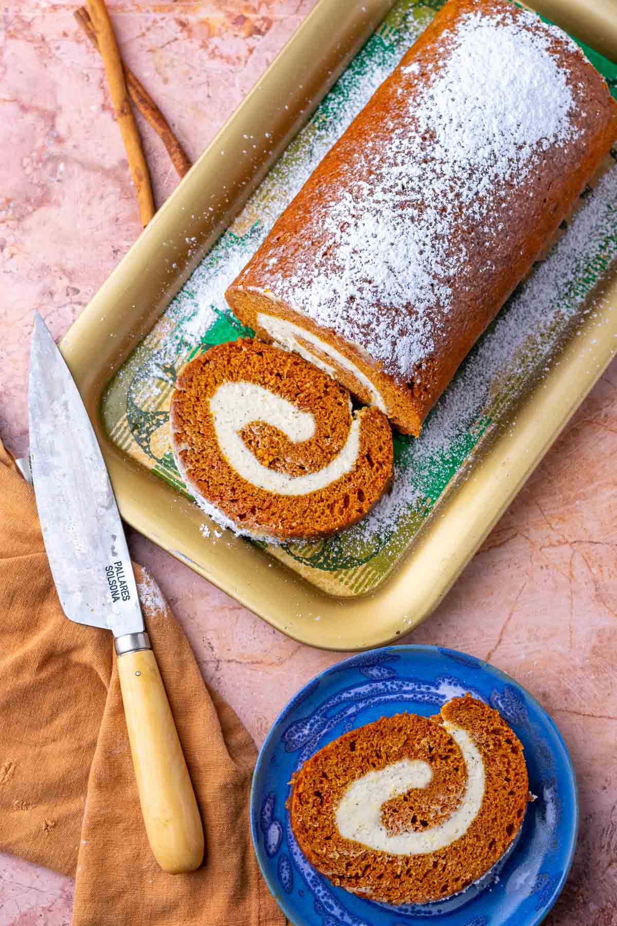 Overhead of sourdough pumpkin roll on a platter and a slice on a plate with a knife and towel.