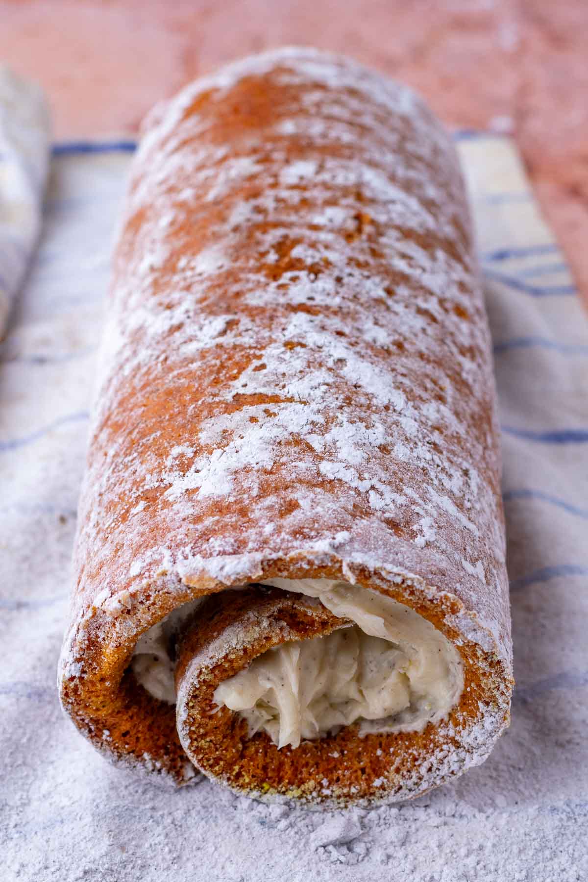 Shaped sourdough pumpkin roll on a towel with powdered sugar.