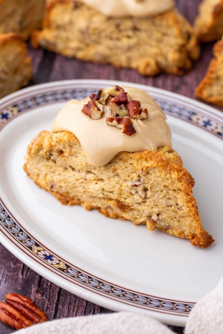 Sourdough maple pecan scone on a plate with a salted maple glaze and pecans on top.
