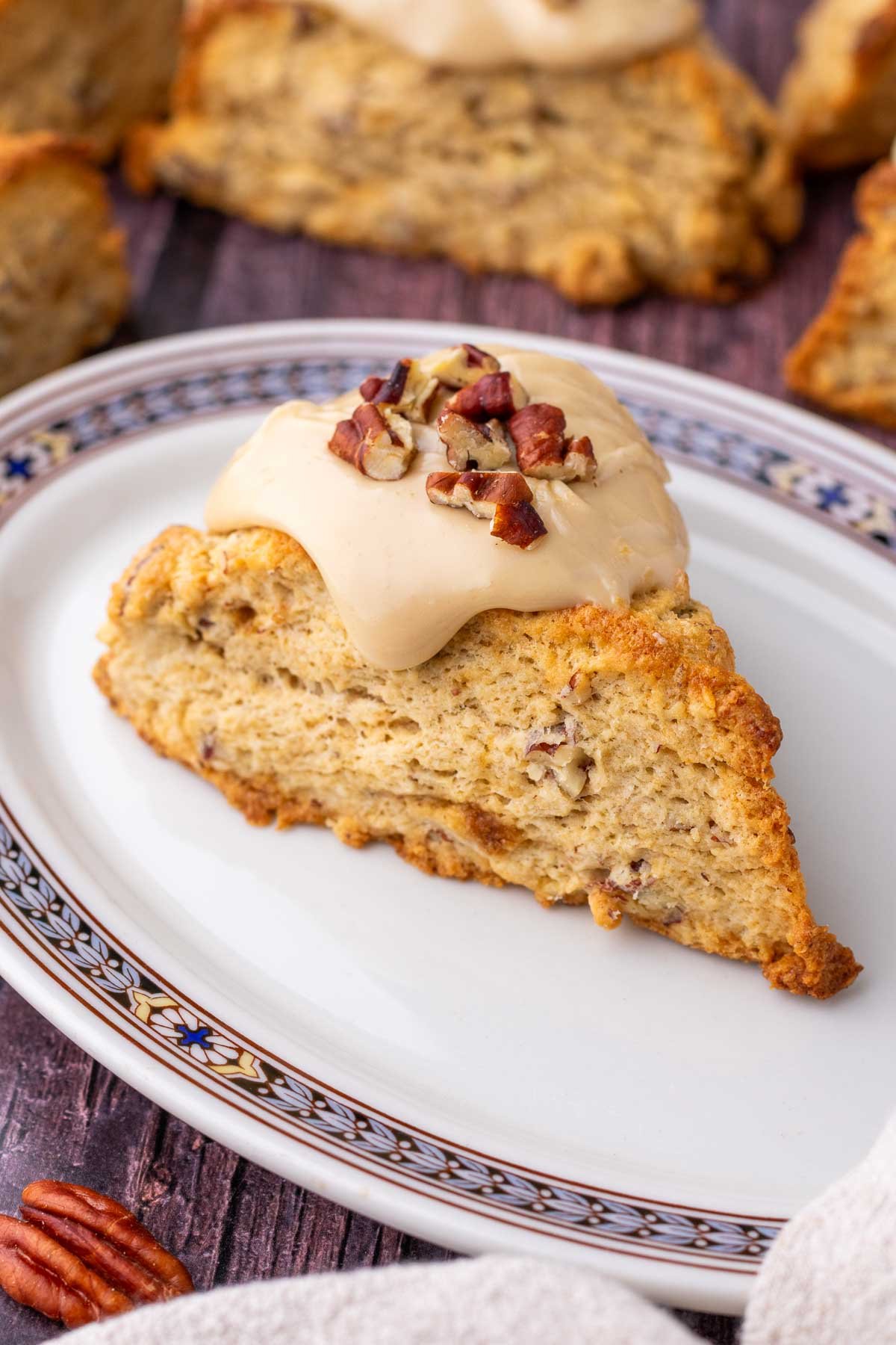 Sourdough maple pecan scone on a plate with a salted maple glaze and pecans on top.