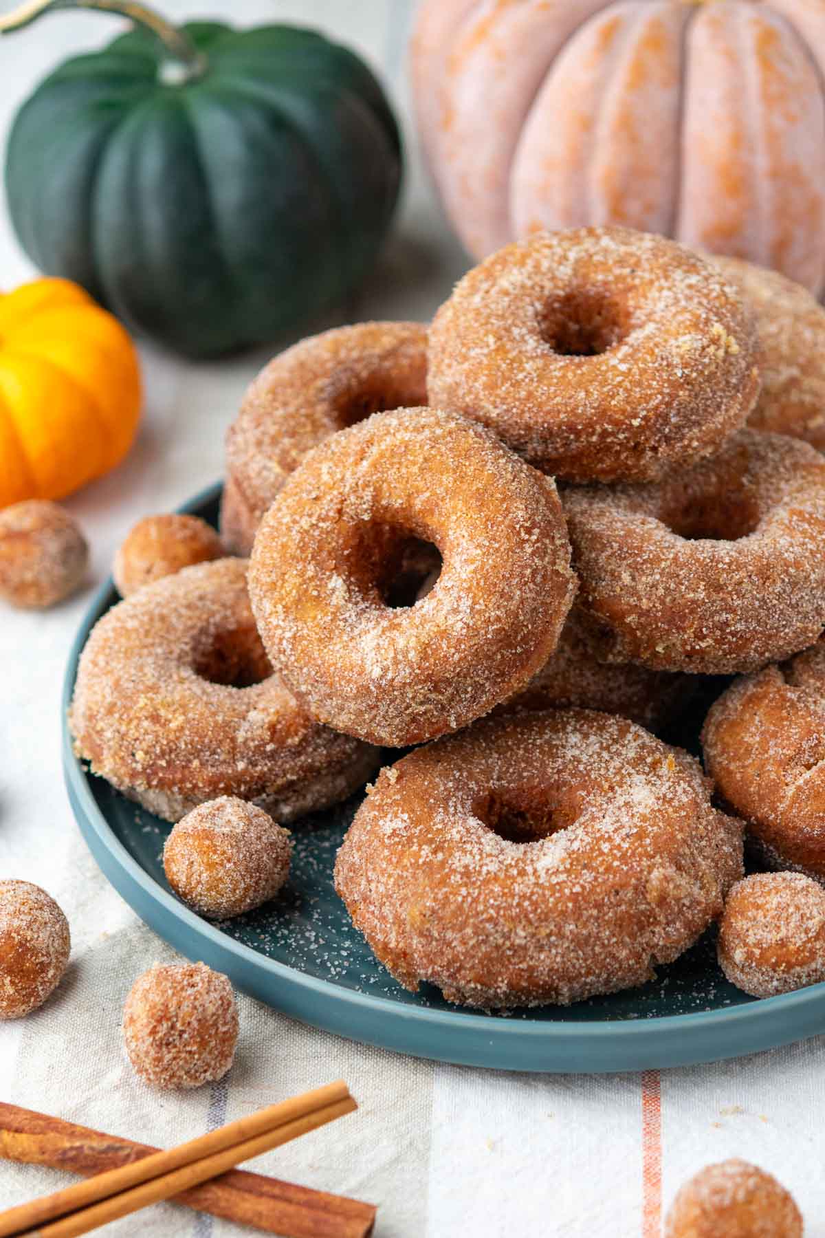 Plate of many sourdough pumpkin donuts stacked on top of each other with pumpkins in the backgroud.