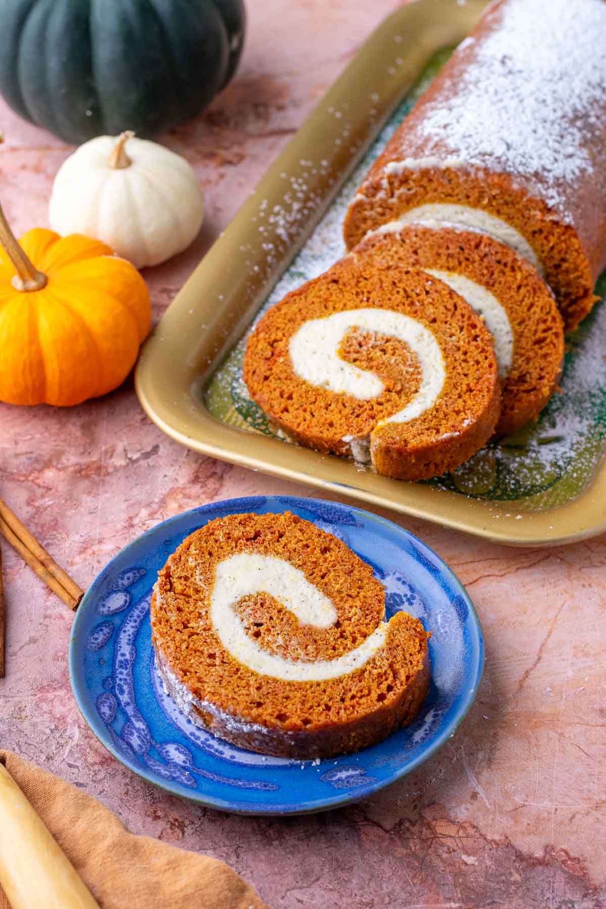 Slices of sourdough pumpkin roll on a plate and platter surrounded by pumpkins.