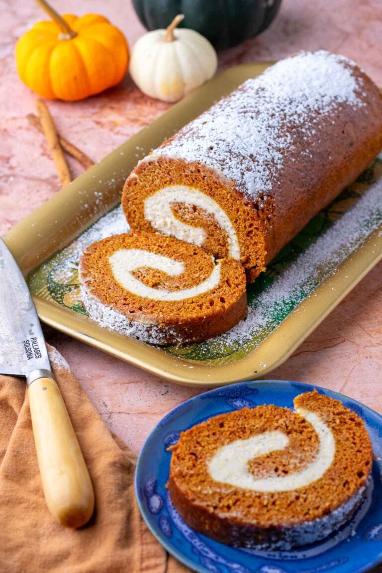 Sliced sourdough pumpkin roll with brown butter cream cheese on a platter and a plate with a knife and pumpkins in the background.