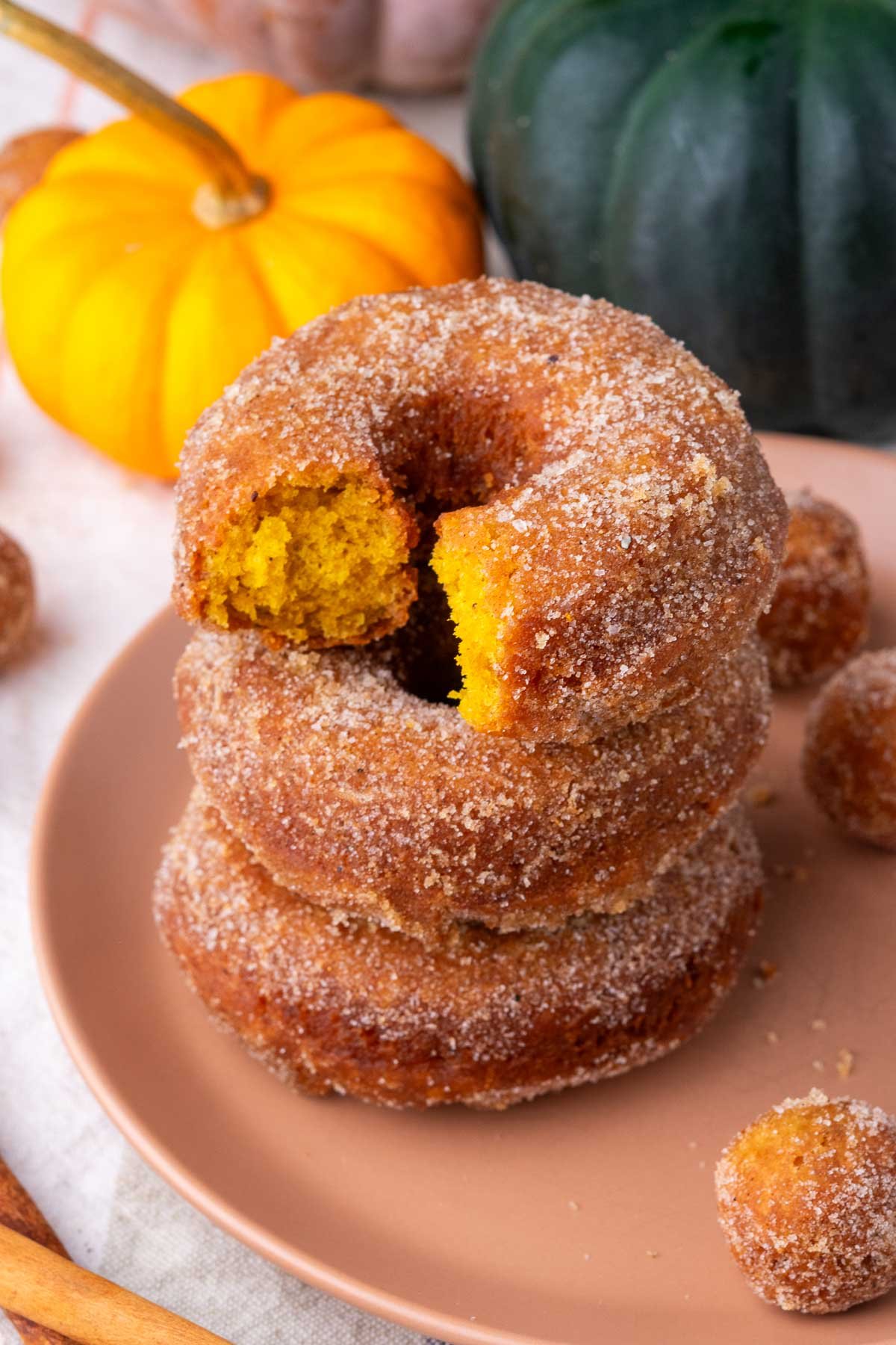 Stack of sourdough pumpkin donuts with a bite taken out of the top one and pumpkins in the background.